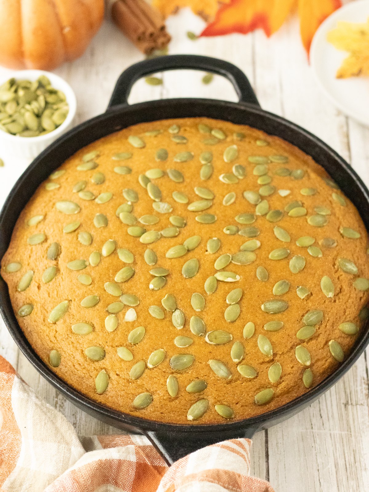 Whole pumpkin cornbread in a cast iron skillet surrounded by fall decorations