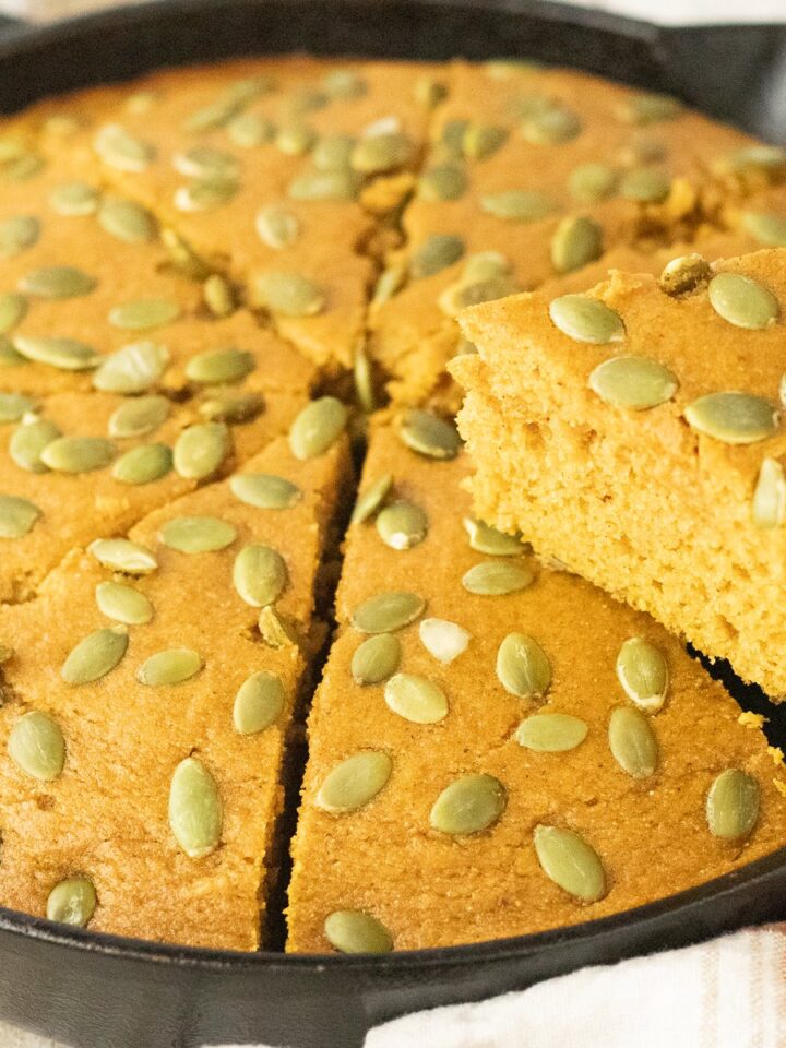 Sliced pumpkin cornbread in a cast iron skillet showing the moist golden crumb