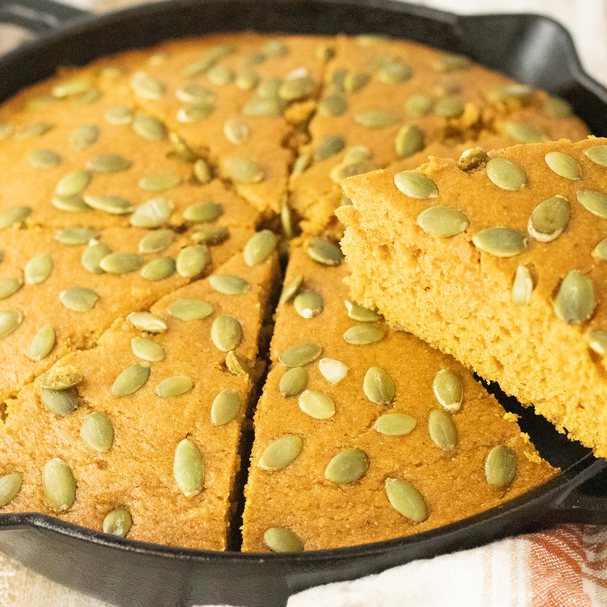 Sliced pumpkin cornbread in a cast iron skillet showing a moist crumb.