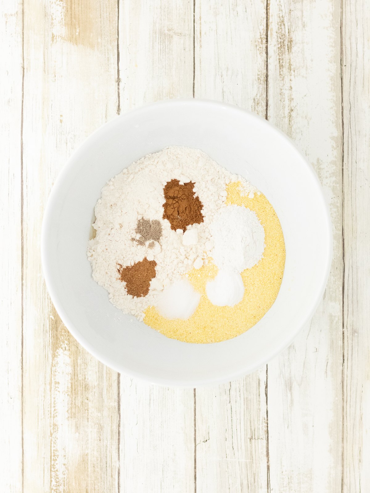 Cornmeal, flour and warm spices whisked together in a white mixing bowl