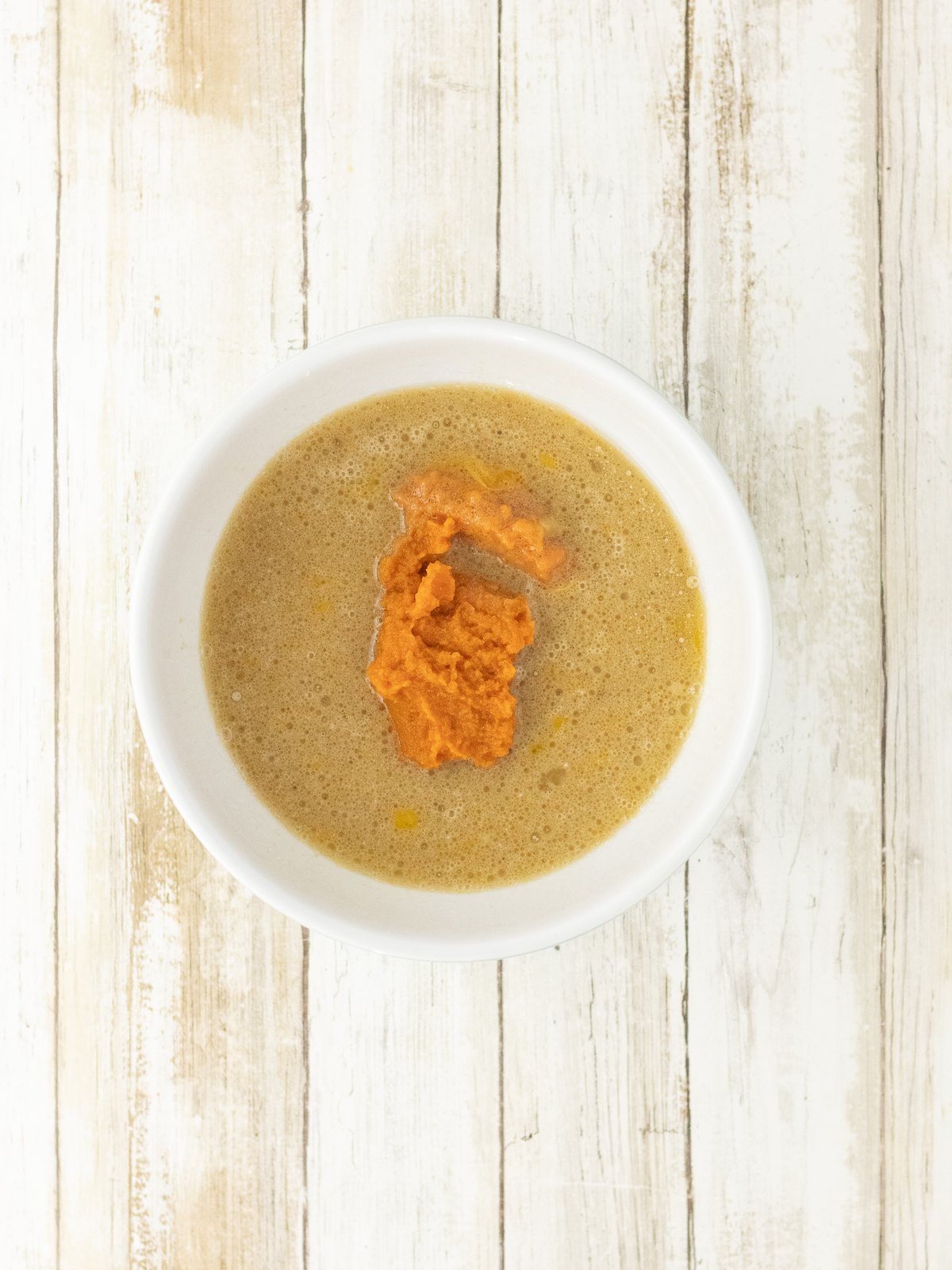 Pumpkin puree being stirred into the wet ingredients for pumpkin cornbread