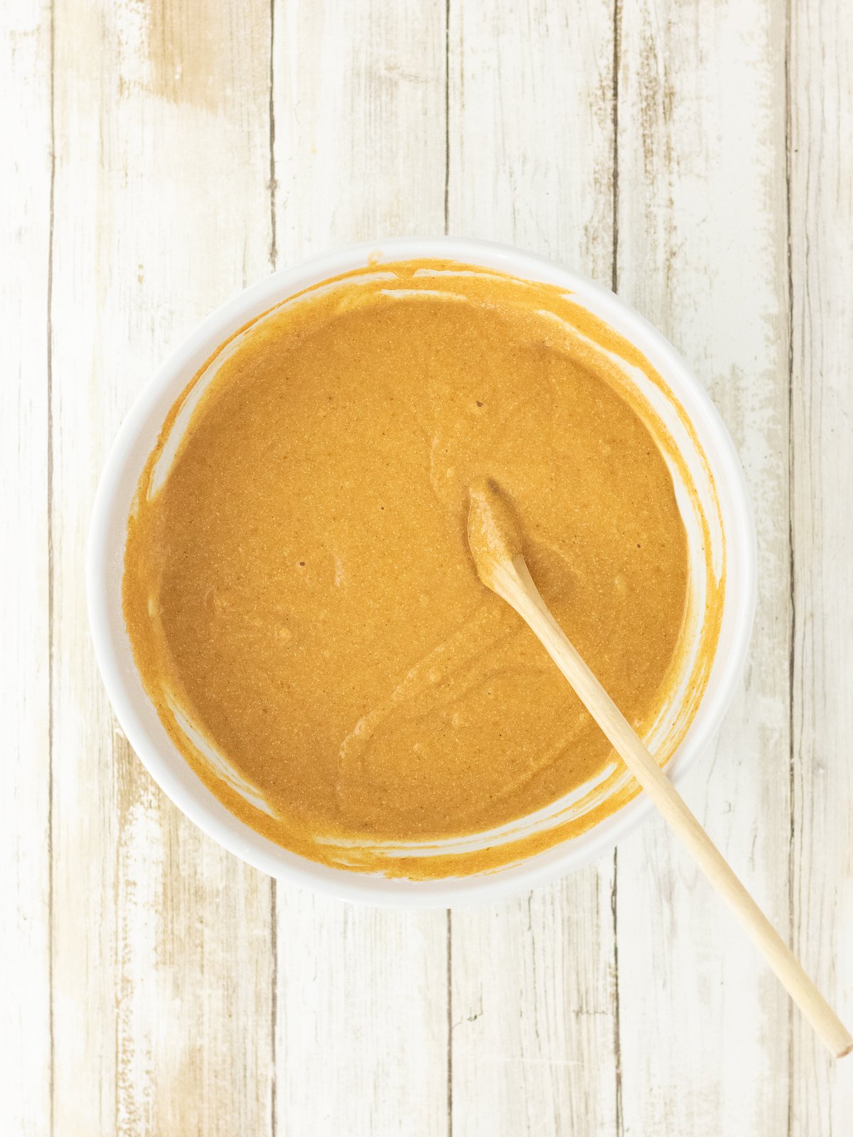 Thick pumpkin cornbread batter mixed by hand with a wooden spoon