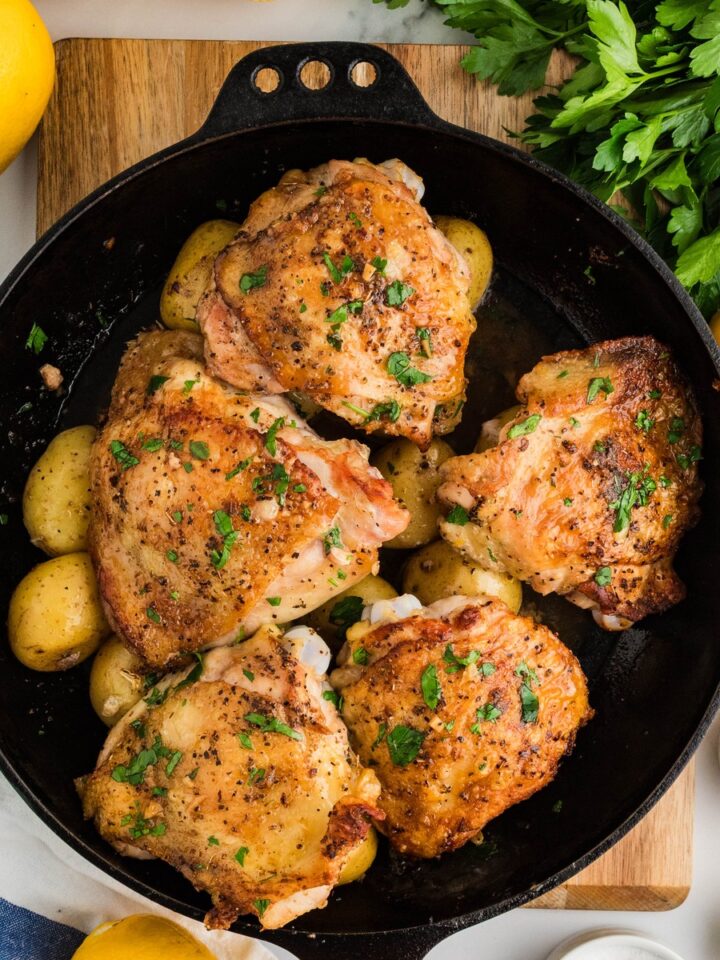 Greek lemon chicken and potatoes in a cast iron skillet garnished with parsley and lemon