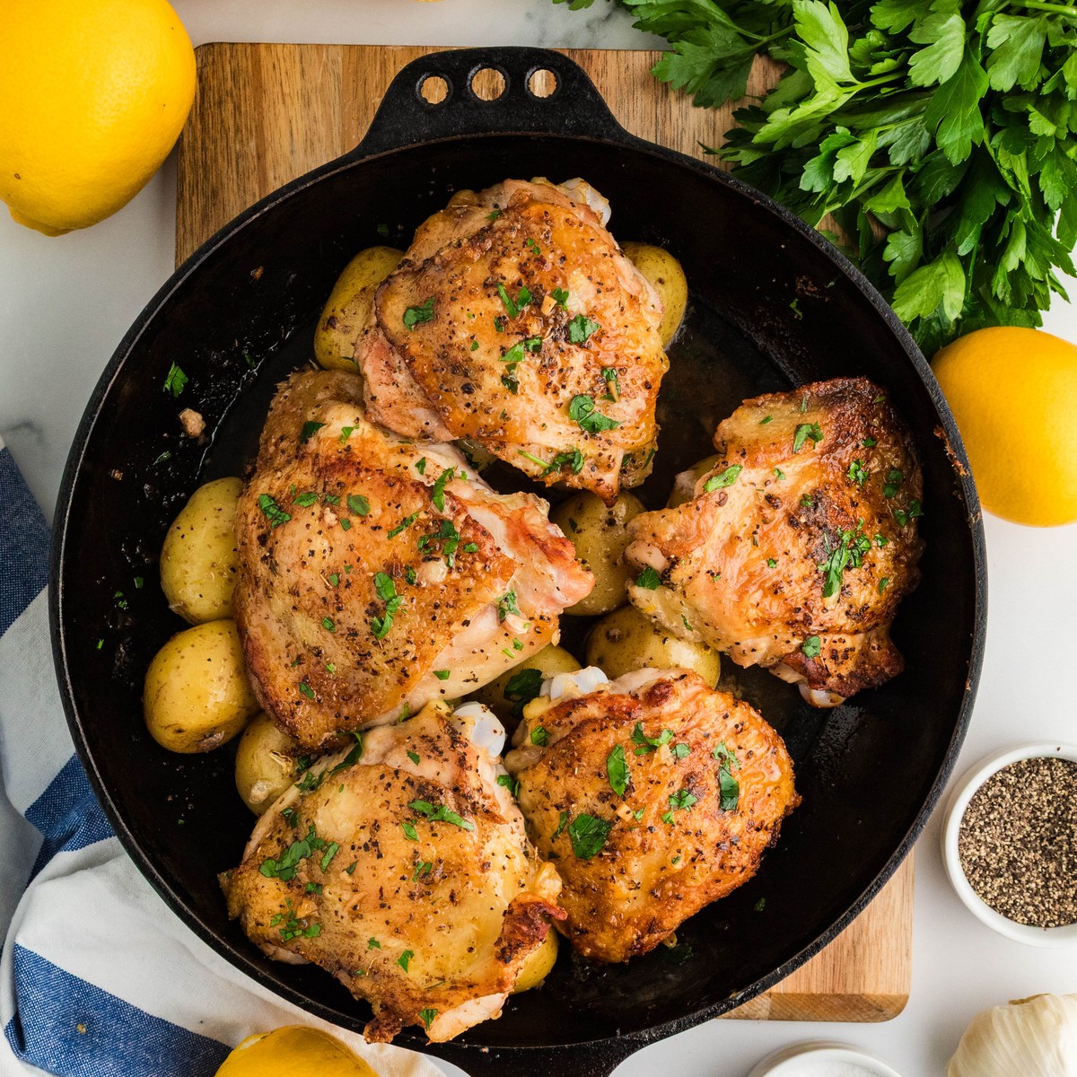 Greek lemon chicken and potatoes in a cast iron skillet garnished with parsley and lemon