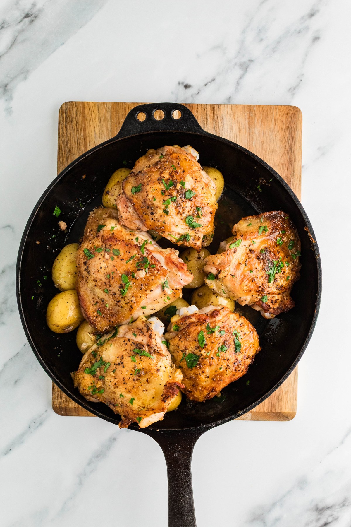 Finished Greek lemon chicken and potatoes garnished with parsley in a cast iron skillet