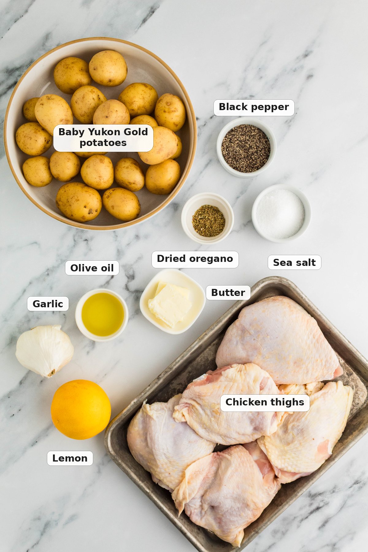 Labeled ingredients for Greek lemon chicken and potatoes on a marble surface