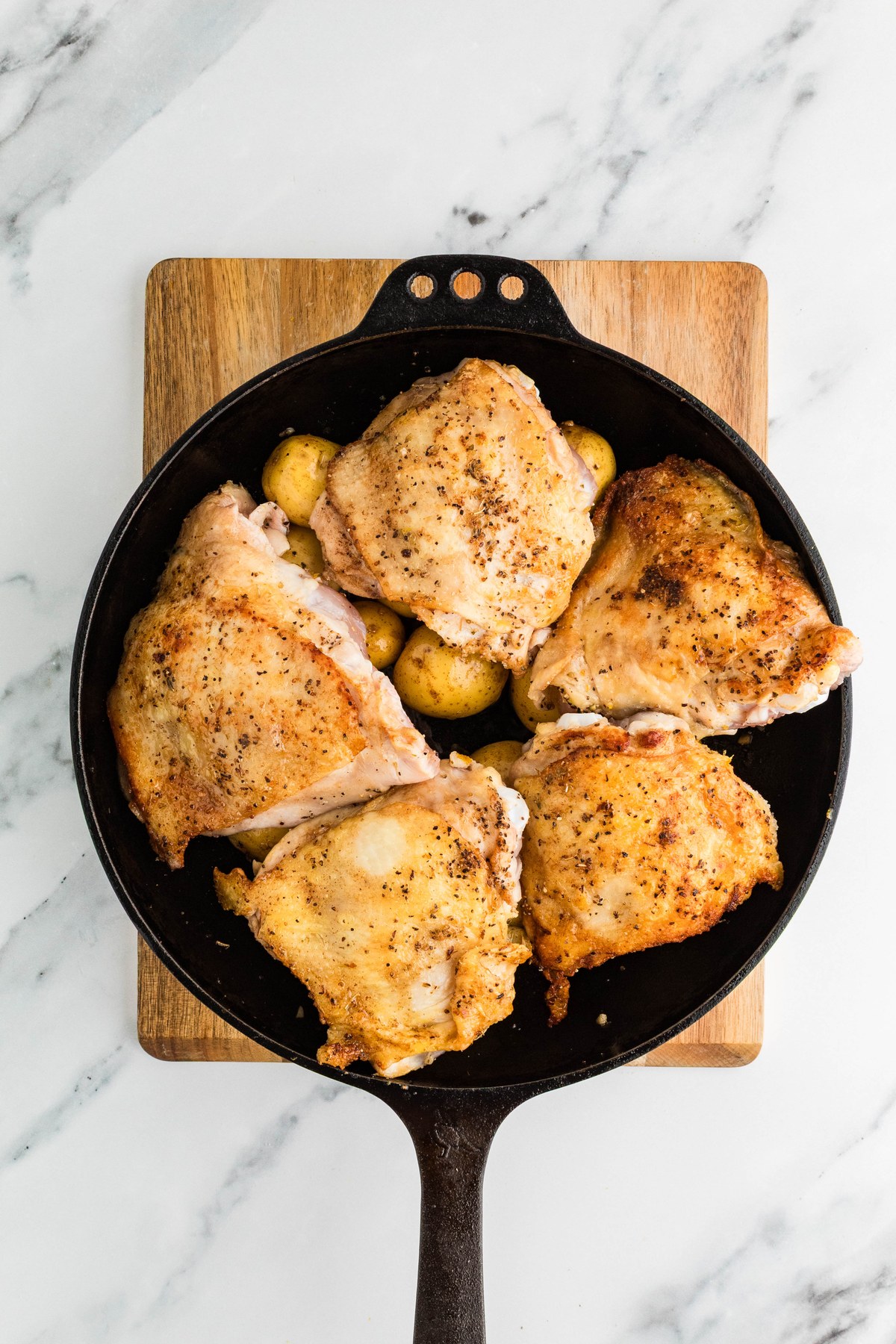 Seared chicken thighs placed over baby potatoes in a skillet before roasting