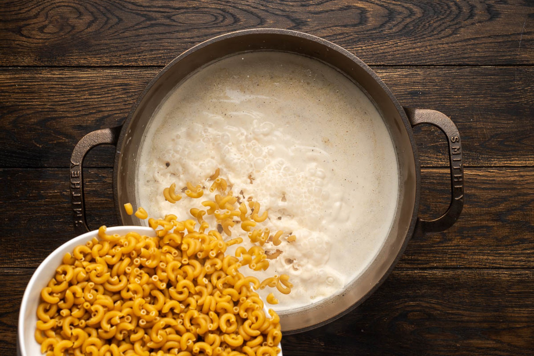 Adding elbow pasta to the simmering liquid in a cast iron pot