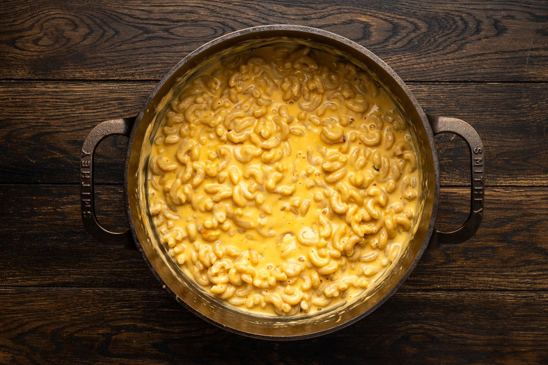 Stirring melted sharp cheddar and pepper jack into the cooked pasta
