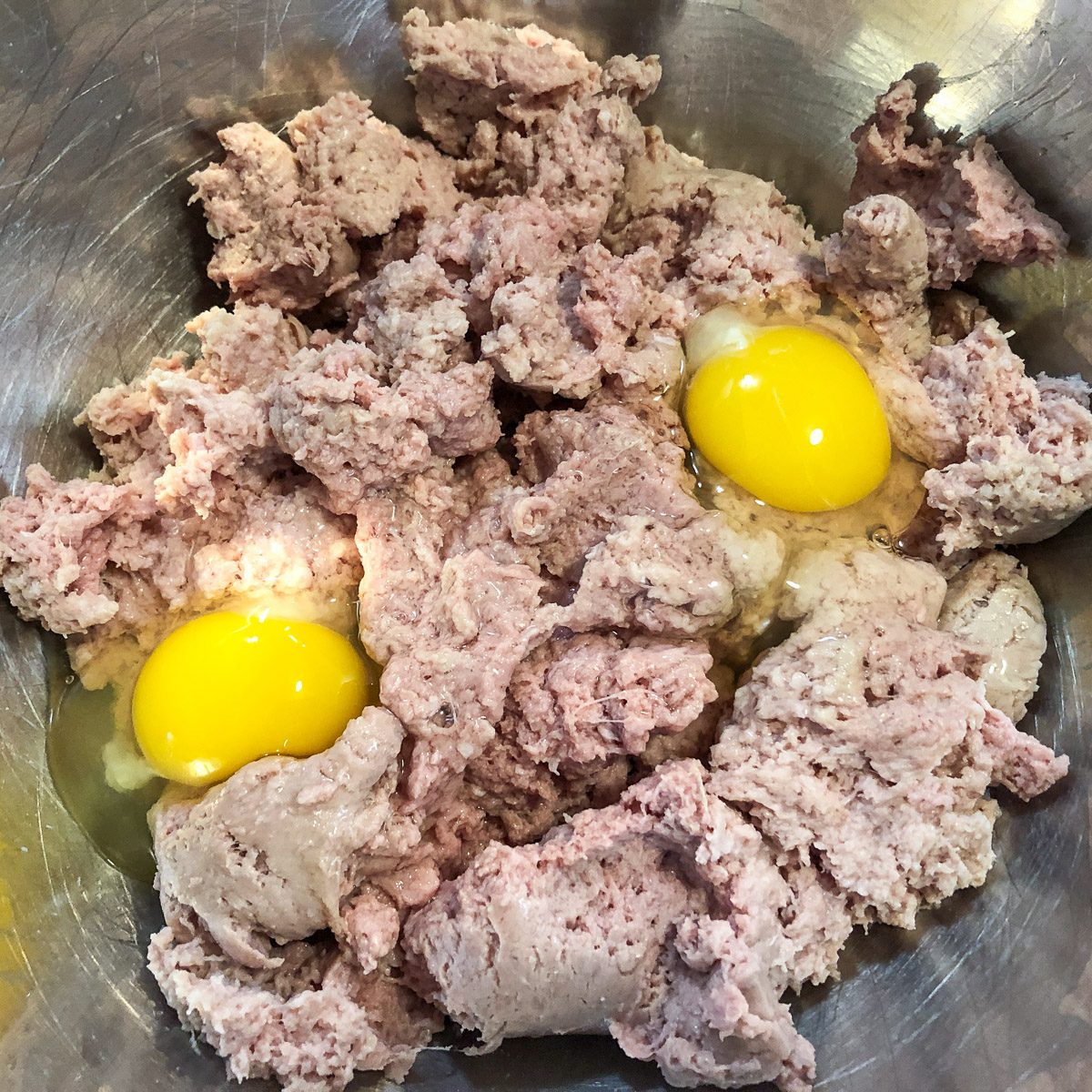 Two eggs cracked into the ground turkey and sausage mixture.