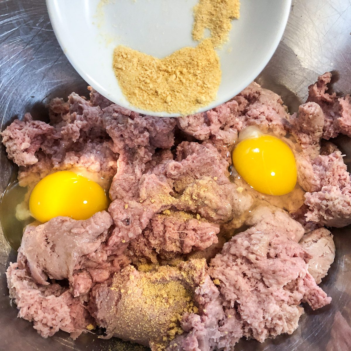 Granulated garlic and seasonings being added to the meat and egg mixture.