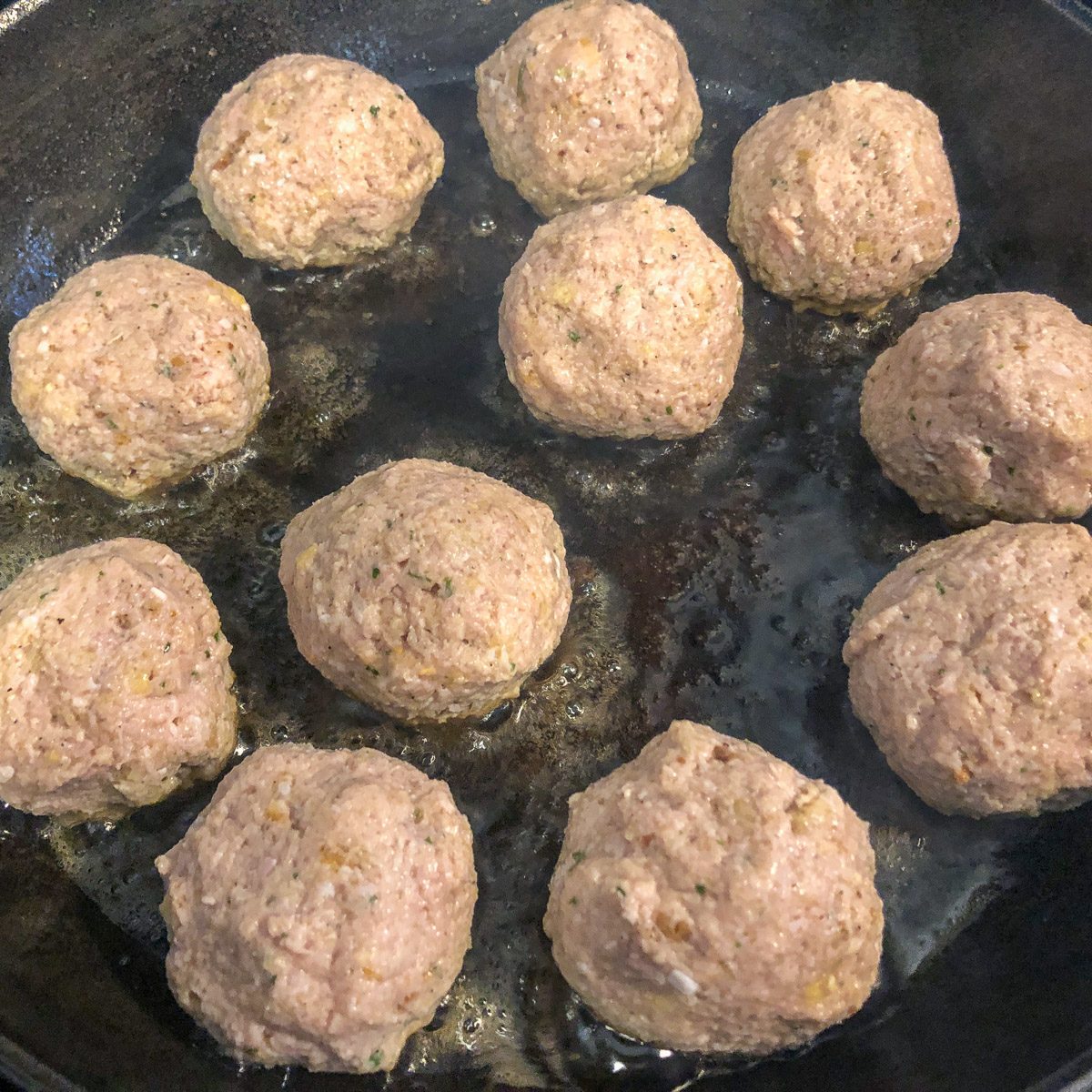 Nine shaped turkey and stuffing meatballs arranged in a cast iron skillet before browning.