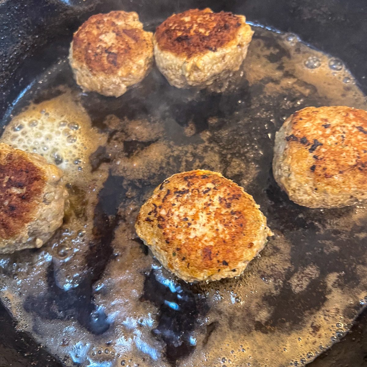 Turkey and stuffing meatballs simmering in a cast iron skillet, one turned to show the golden crust.