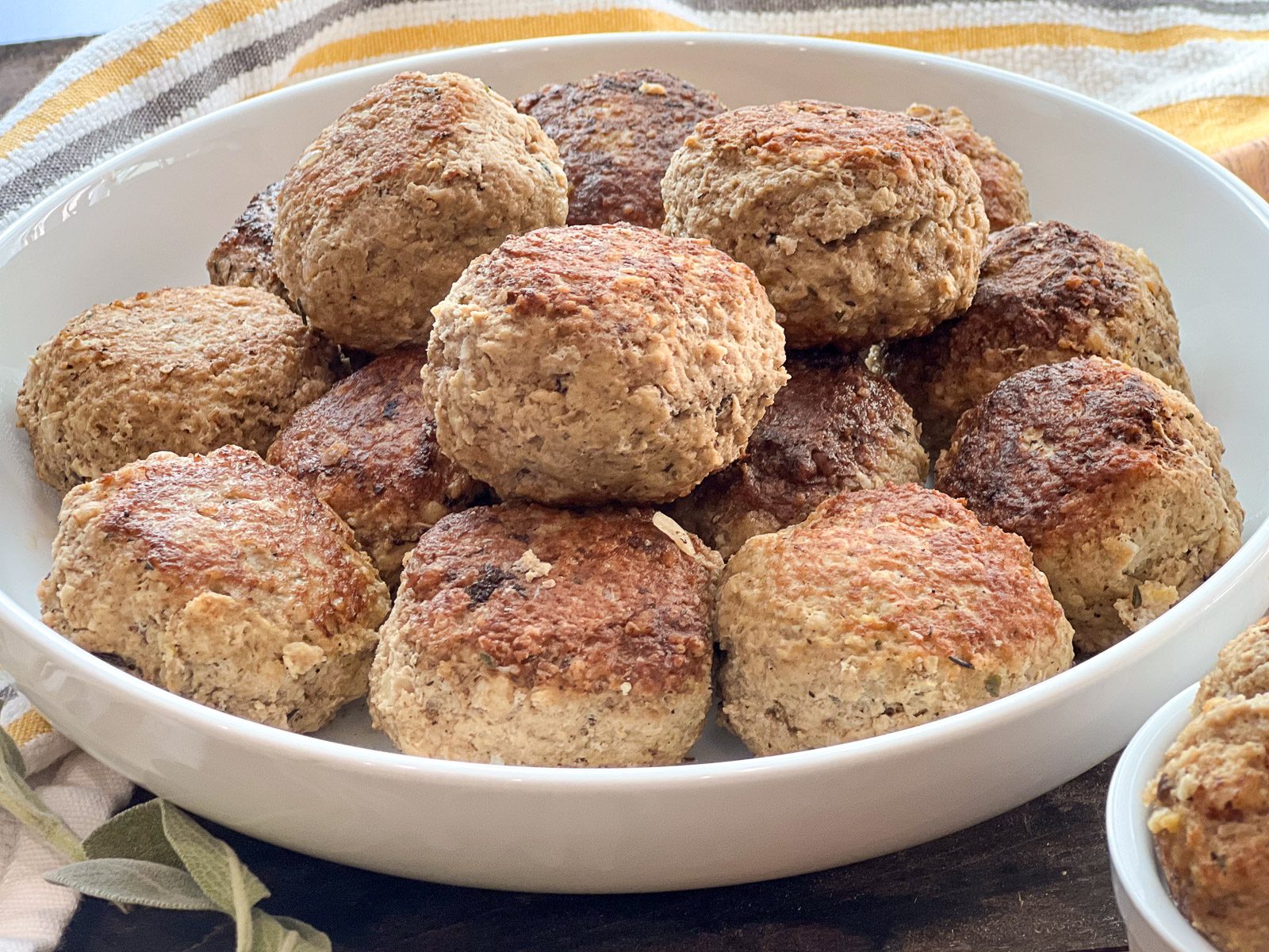 Finished turkey and stuffing meatballs piled in a white serving bowl with fresh sage.