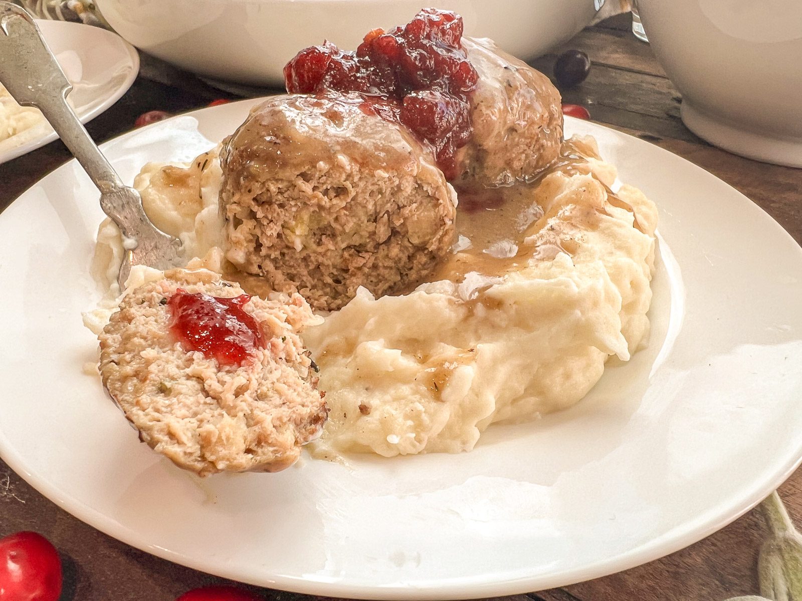 A fork holds a slice of meatball to show the moist interior, topped with a dollop of cranberry sauce.