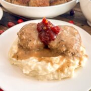 A turkey and stuffing meatball served over mashed potatoes with pan gravy and a spoonful of cranberry sauce.