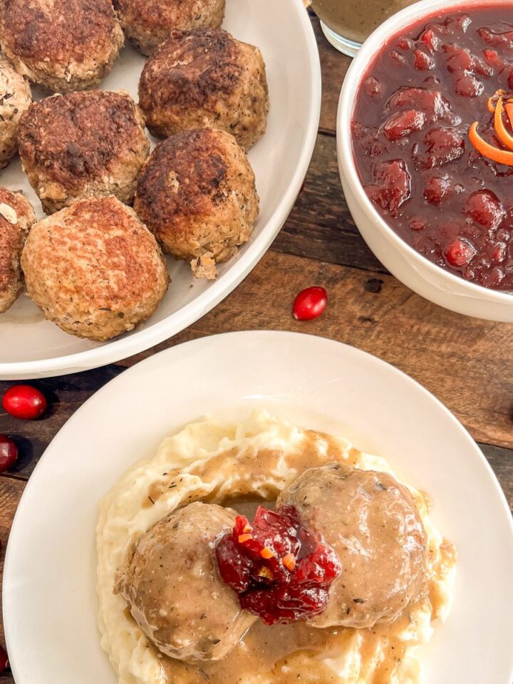 Turkey and stuffing meatballs served over mashed potatoes with gravy and cranberry sauce, with a bowl of meatballs and a dish of cranberry sauce alongside.