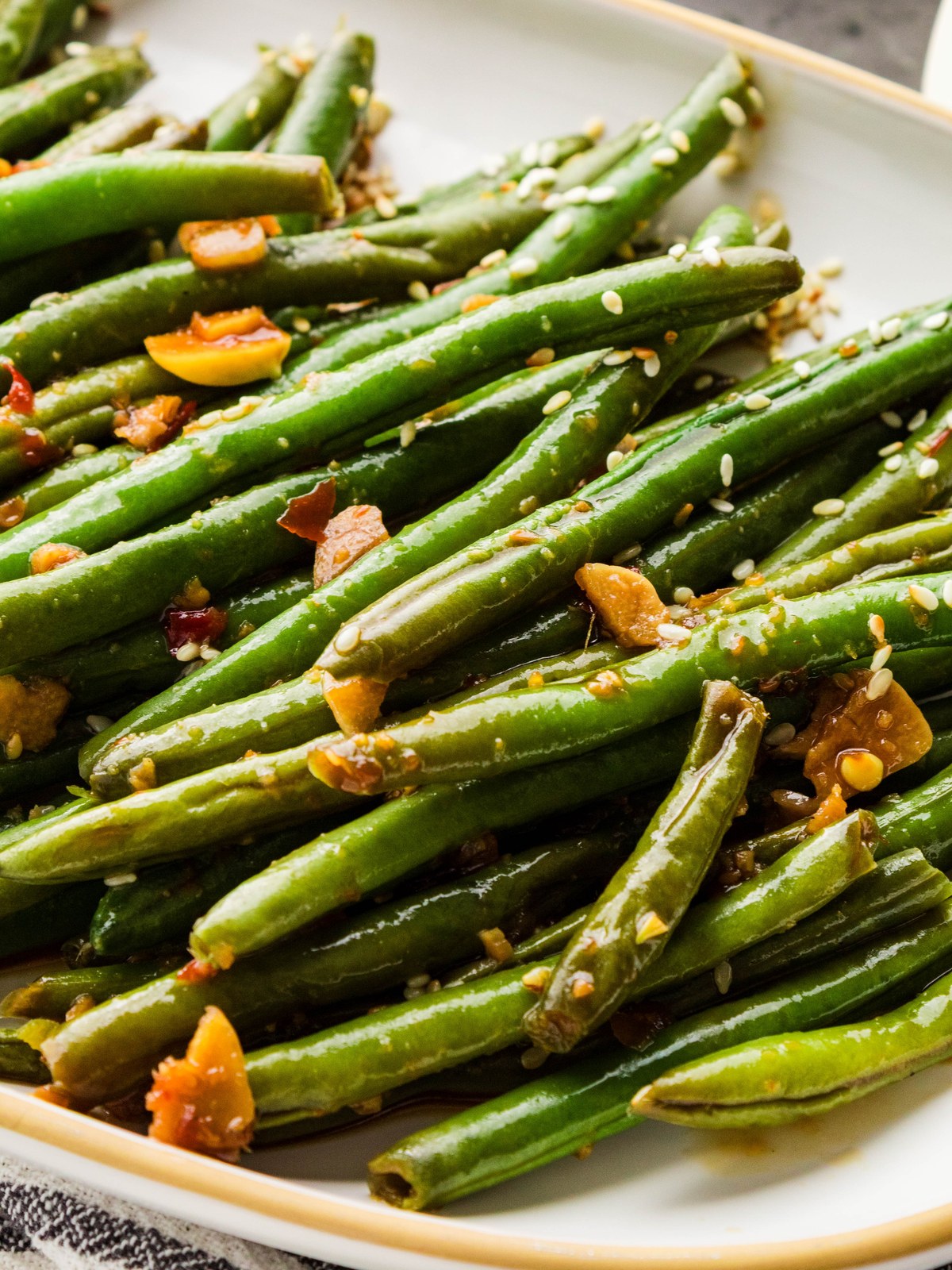 Asian green beans on a white platter topped with sliced garlic and sesame seeds