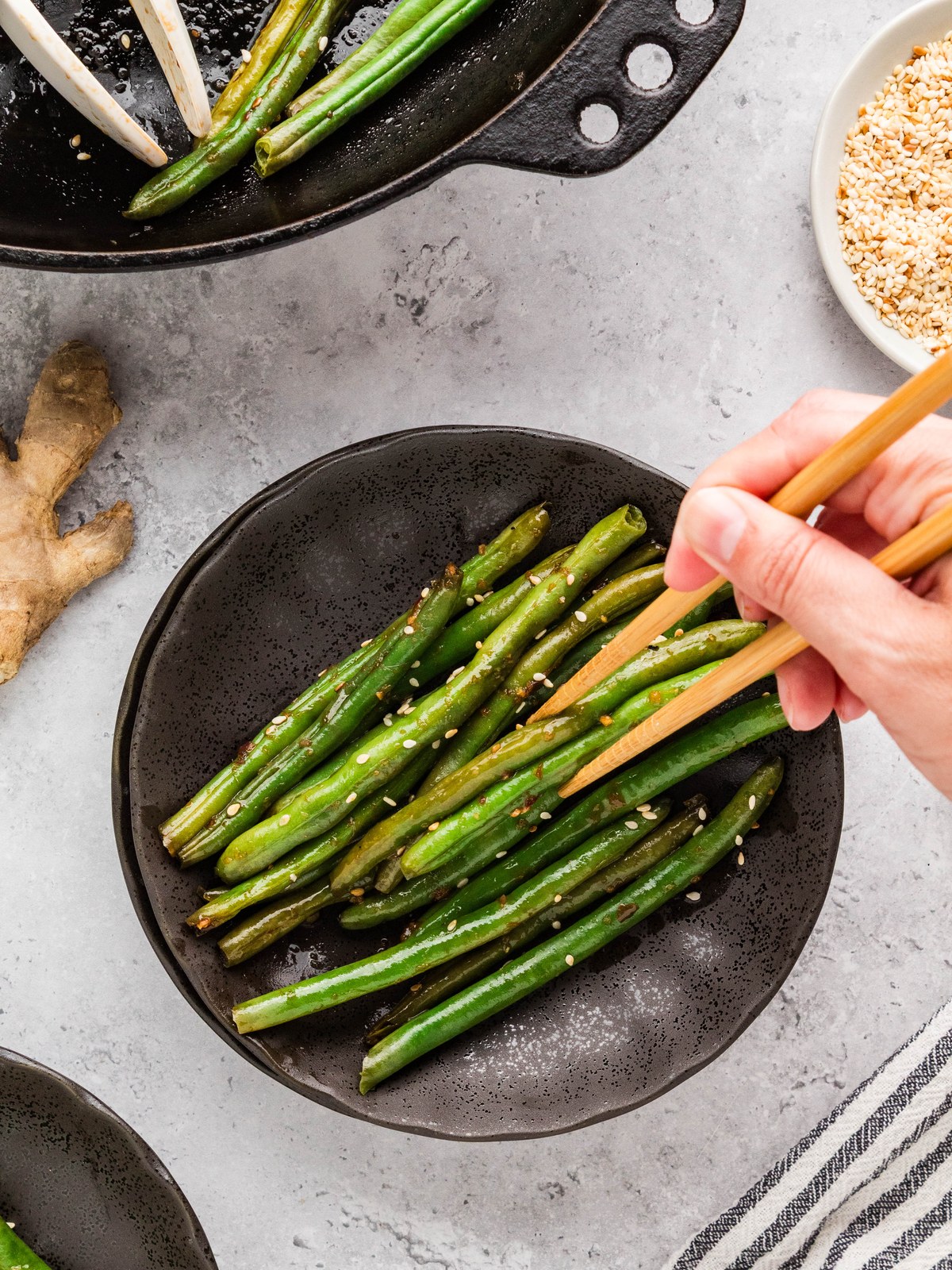 Serving Asian green beans onto a dark plate with chopsticks