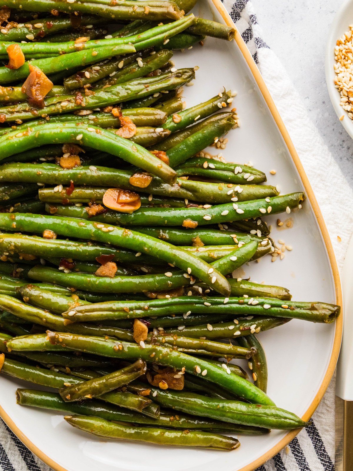 Asian green beans arranged on a white serving platter with toasted sesame seeds