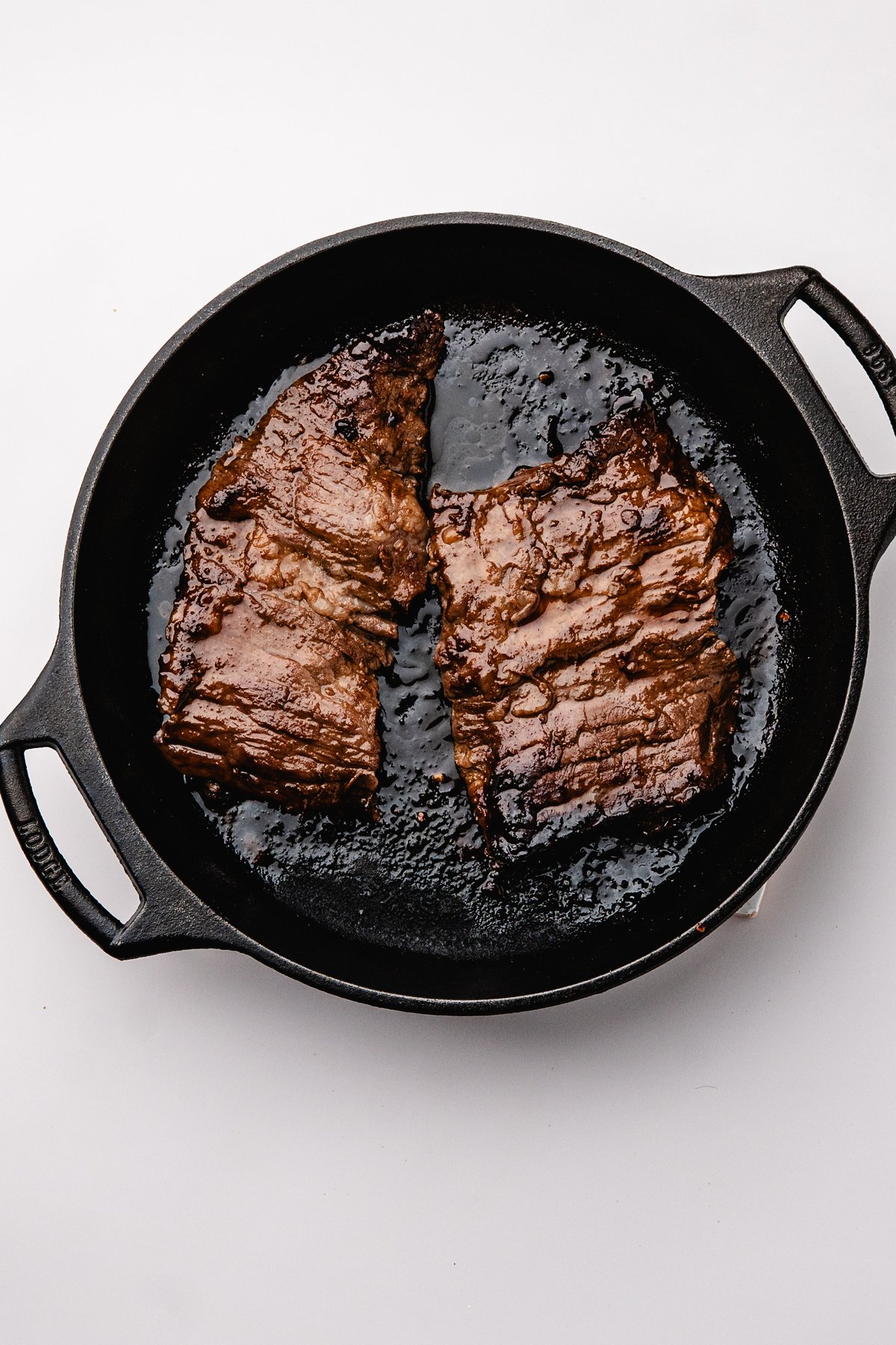 Seared marinated steak with a dark browned crust in a cast iron skillet