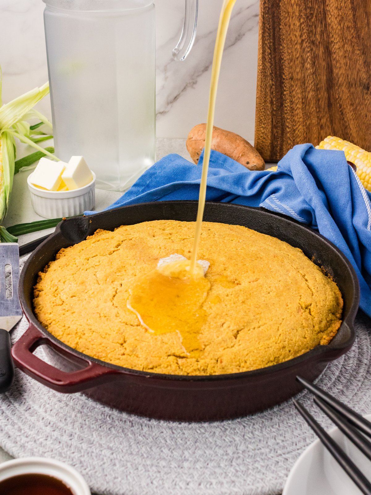 Brown butter maple glaze being poured over sweet potato cornbread in a cast iron skillet