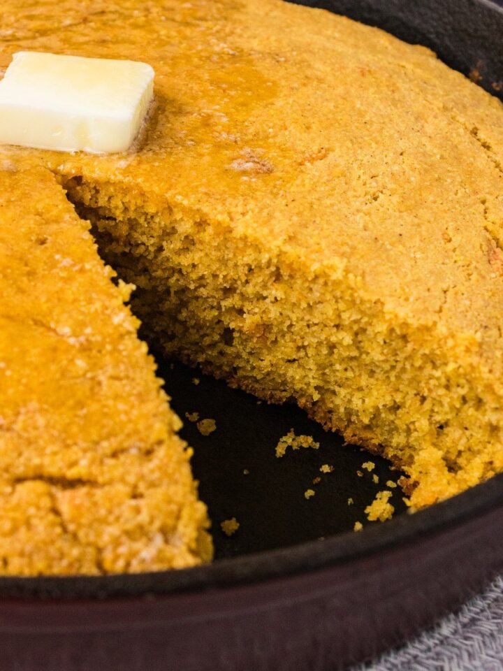 Sweet potato cornbread in a cast iron skillet with one wedge cut out and a pat of butter melting on top