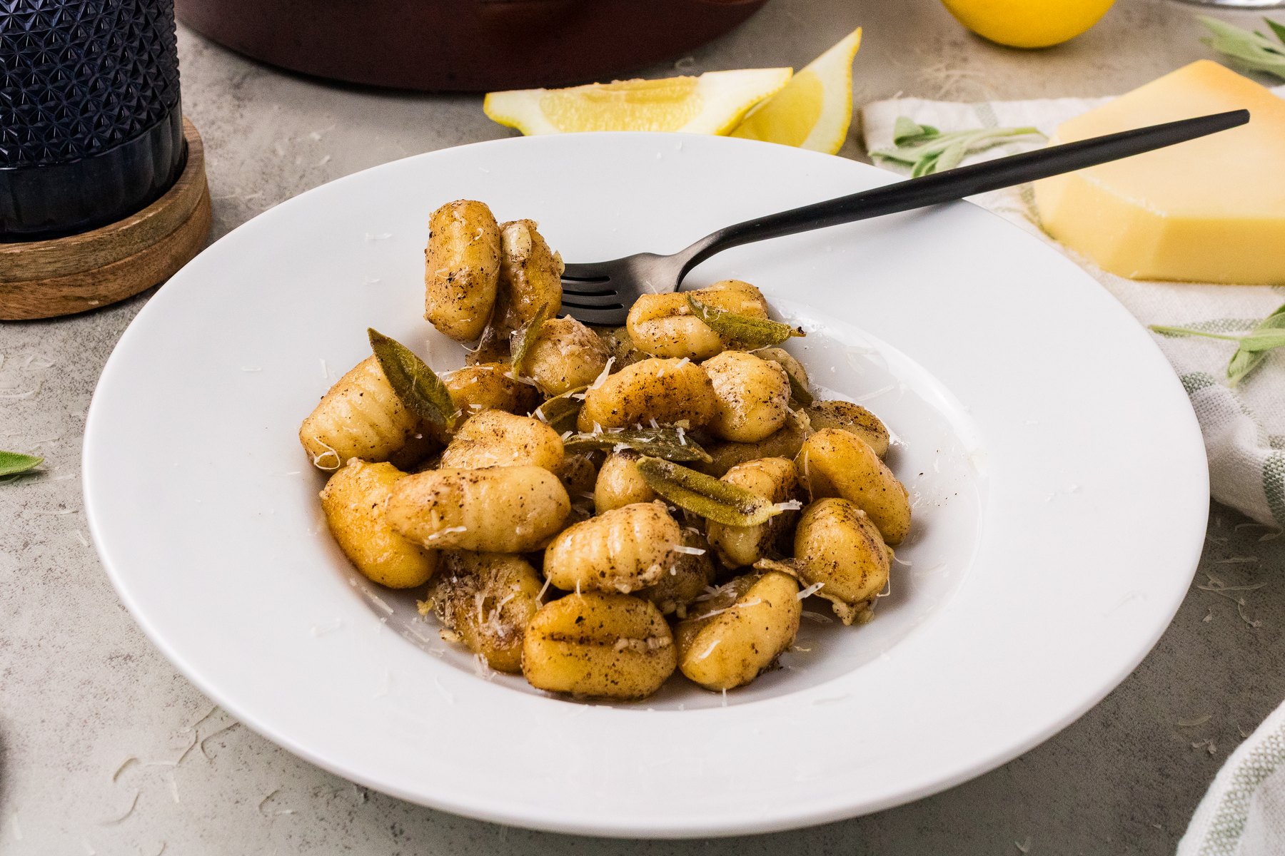Plated brown butter sage gnocchi with a black fork, lemon wedges and Parmesan