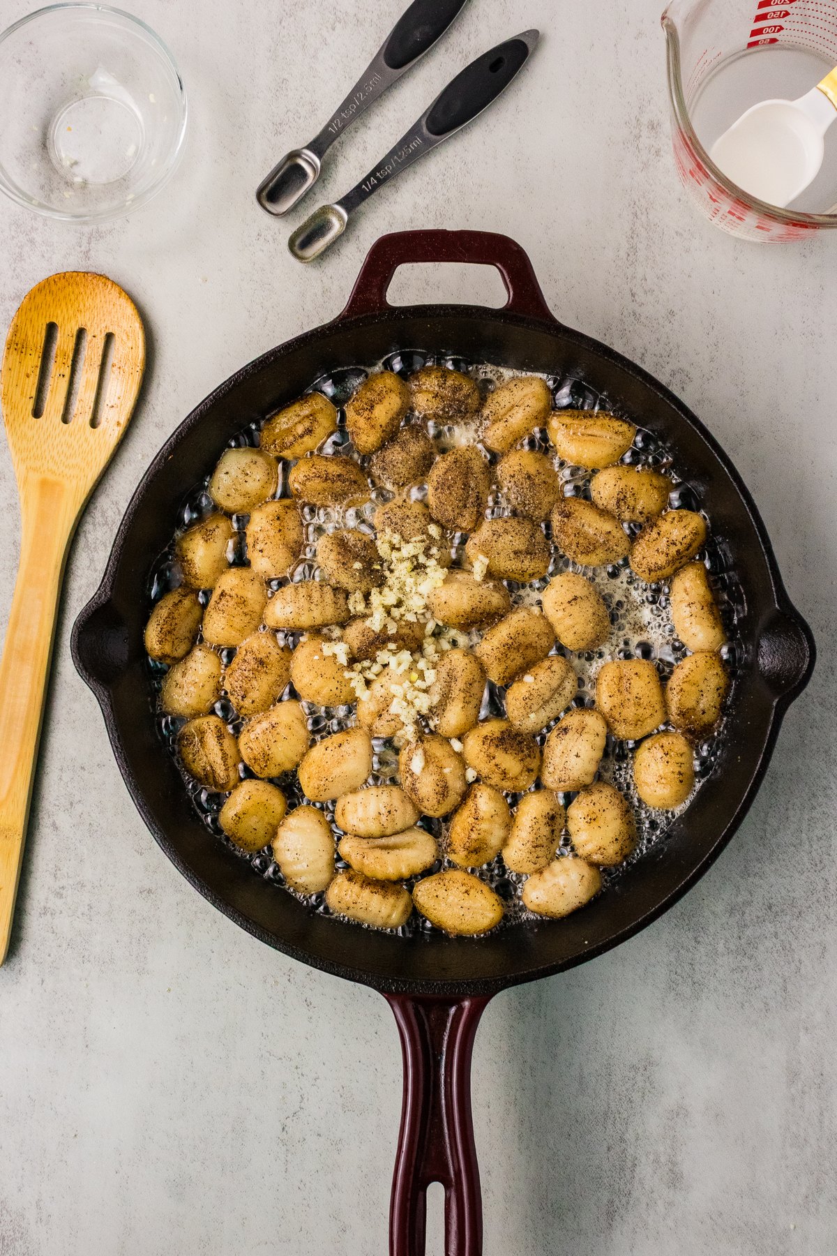 Minced garlic added to golden brown gnocchi in a cast iron skillet