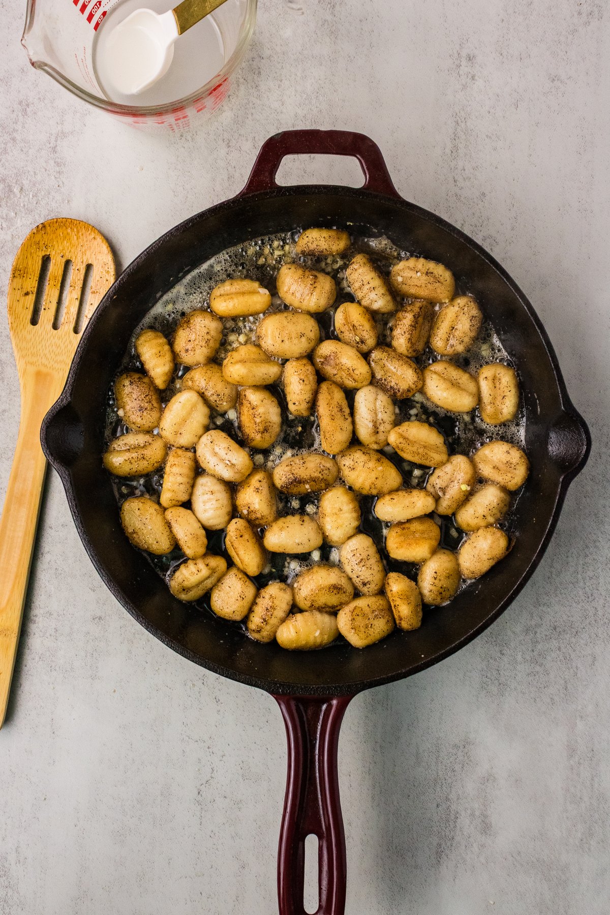 Reserved gnocchi cooking water added to brown butter in a cast iron skillet