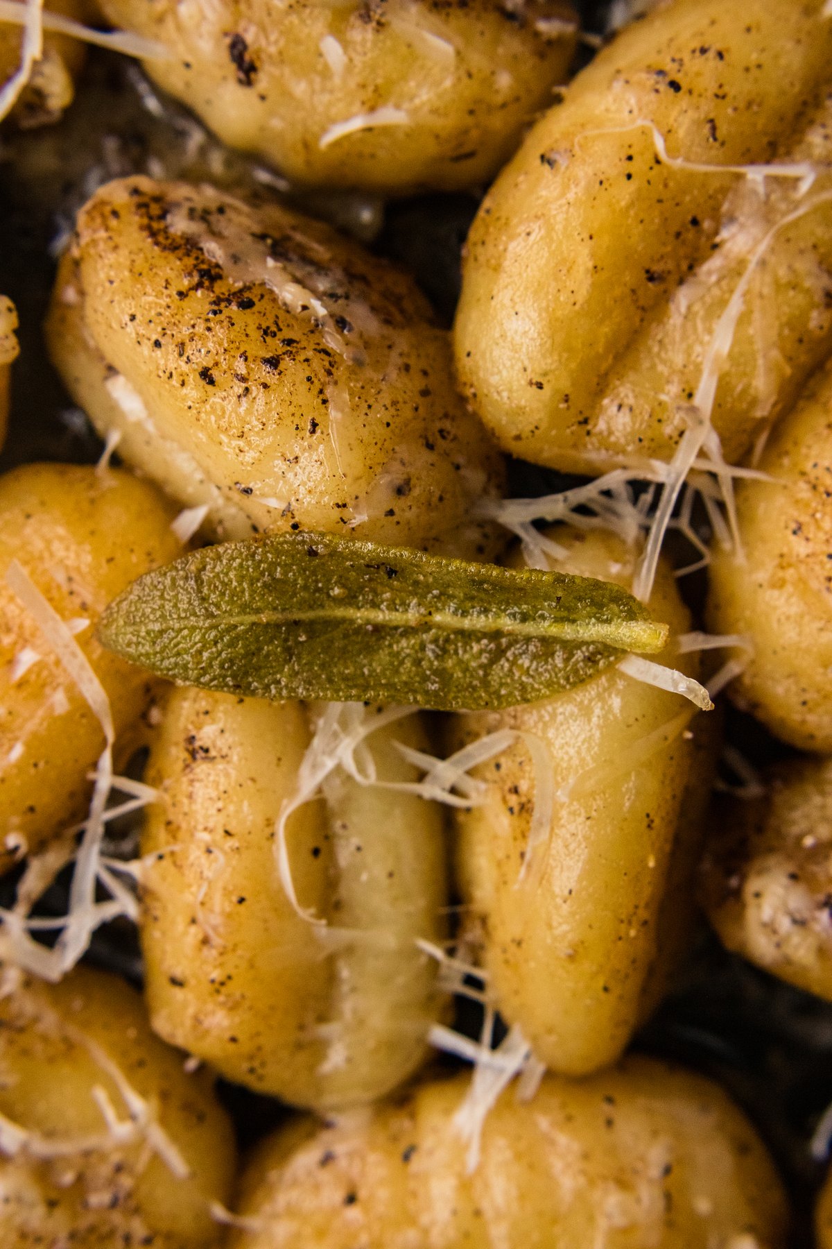 Close up of crispy golden gnocchi with a fried sage leaf and shredded Parmesan