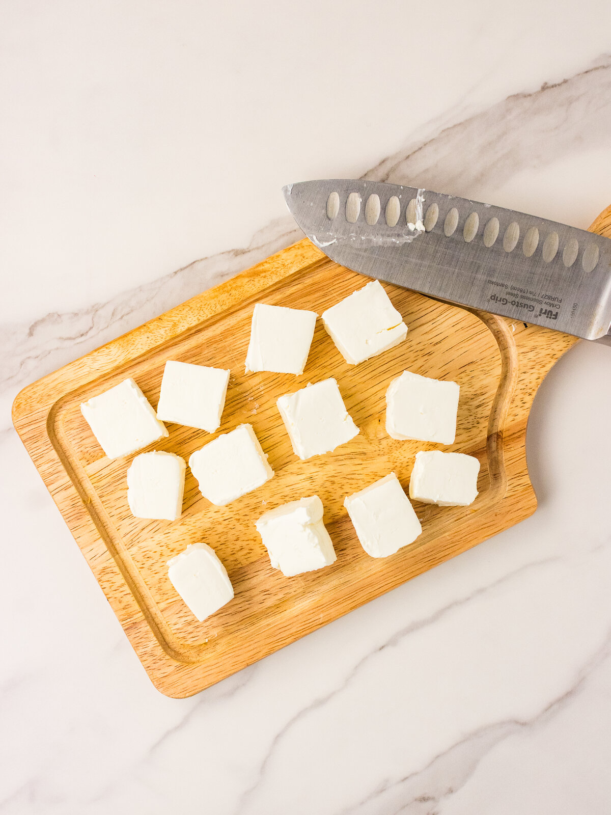 Cubed cream cheese on a wooden cutting board with a knife