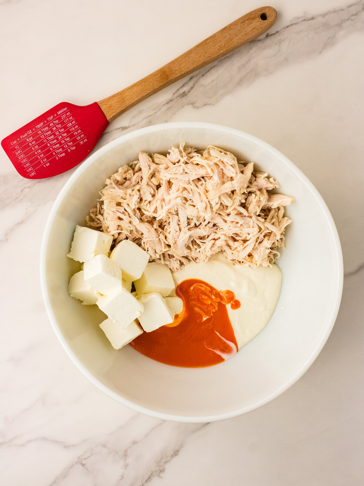 Shredded rotisserie chicken cream cheese ranch and buffalo sauce in a mixing bowl