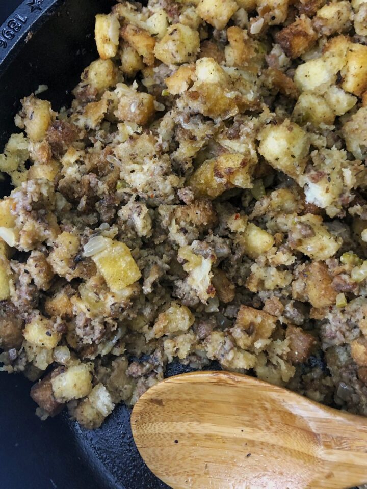 Cast iron skillet full of golden sausage stuffing with a wooden spoon.