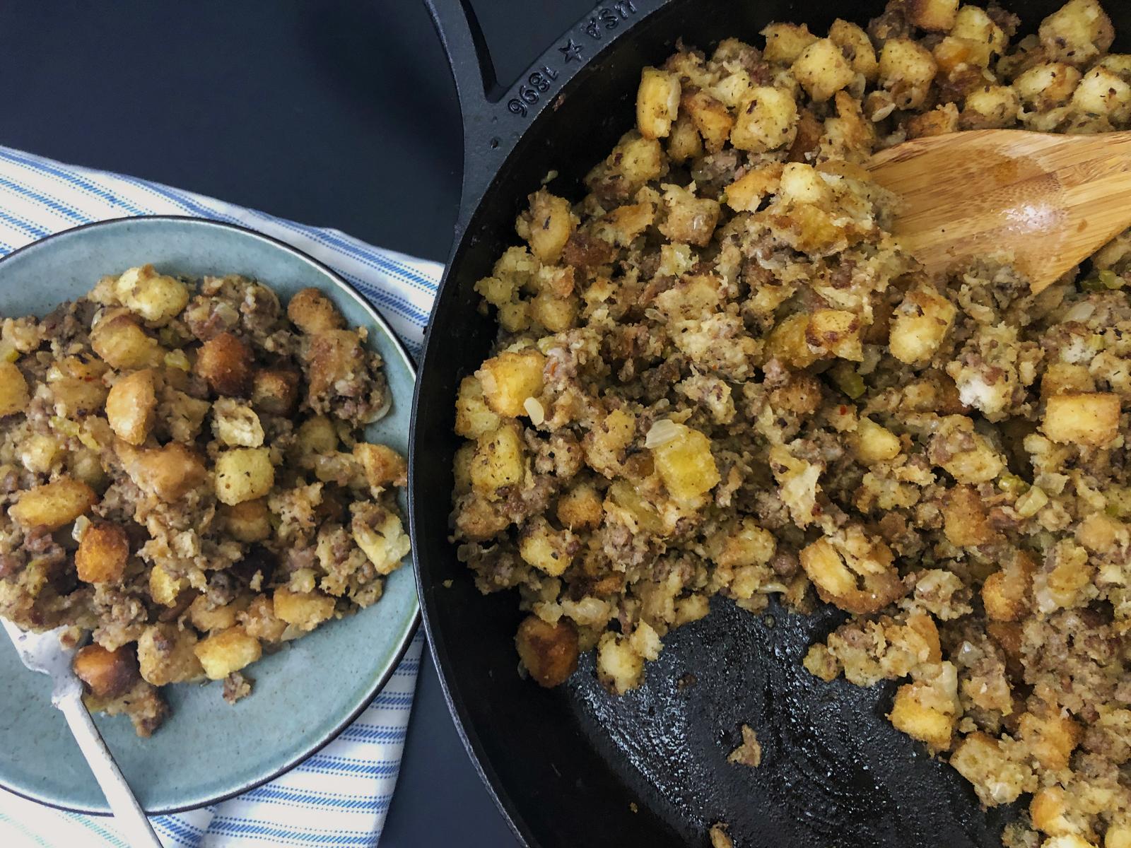 Plate of sausage stuffing with a fork in front of the cast iron skillet.