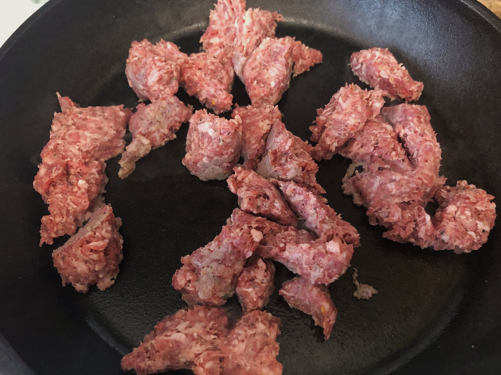 Crumbled sage pork sausage browning in a hot cast iron skillet.