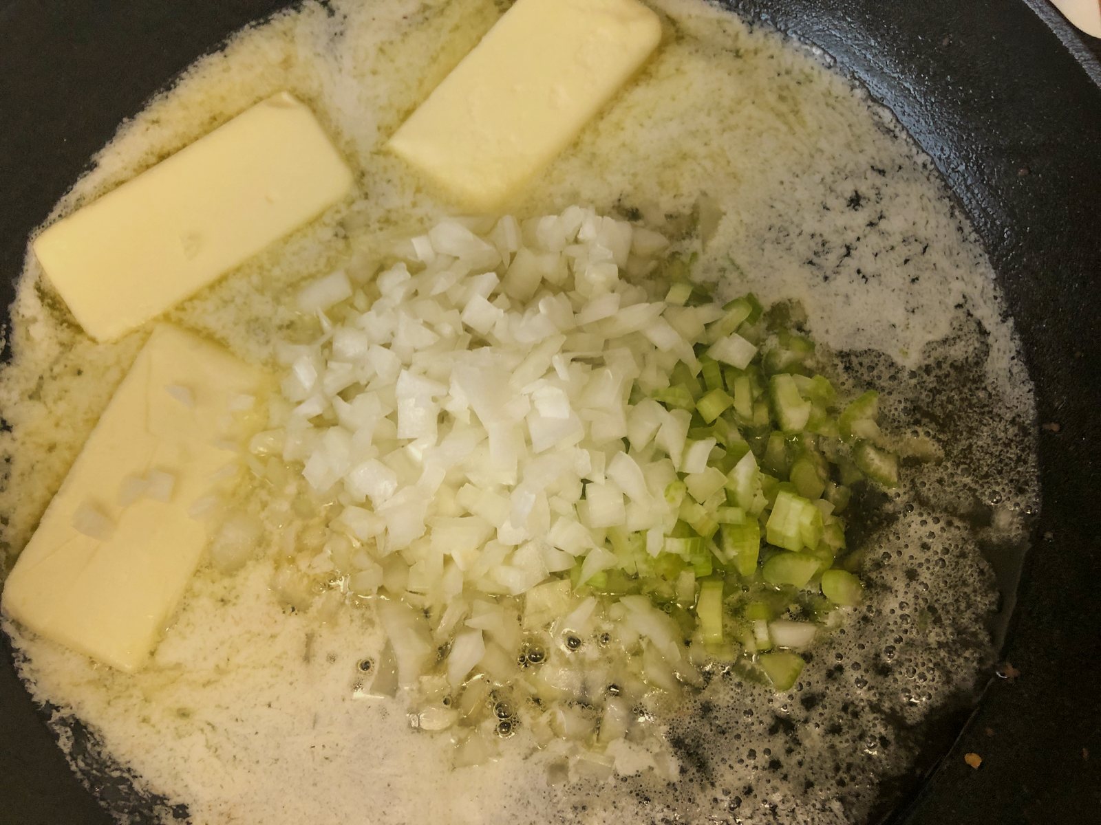 Three sticks of butter melting with diced onion and celery in a cast iron skillet.