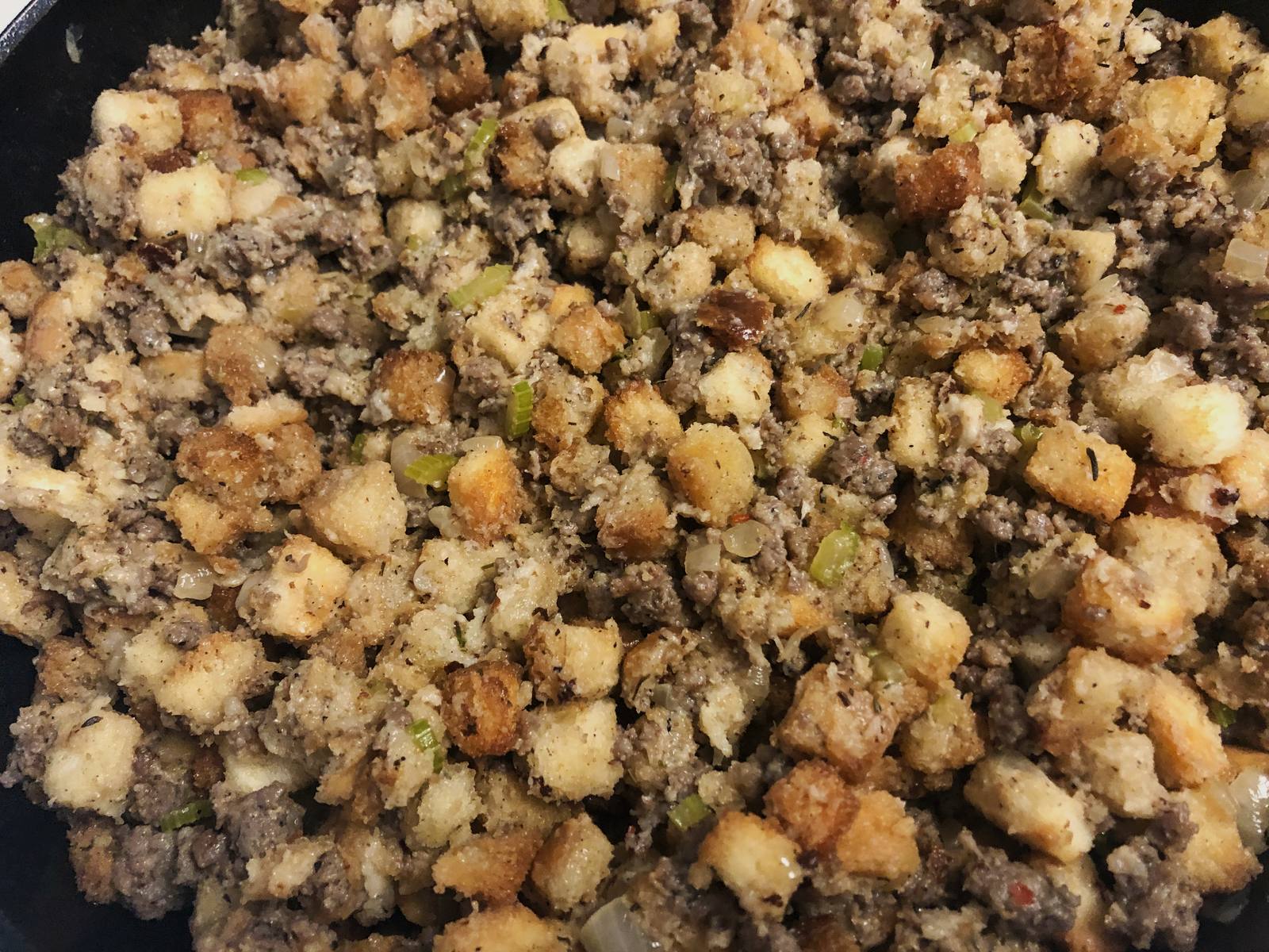 Dried bread cubes and broth mixed into the sausage in the cast iron skillet, ready to bake.