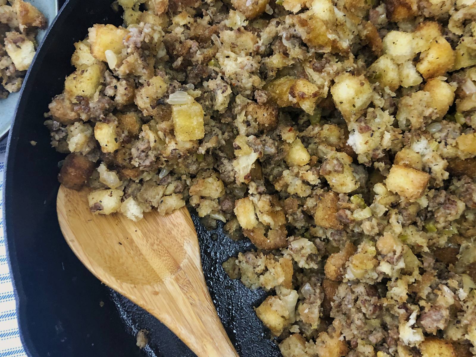 Baked sausage stuffing in a cast iron skillet with a golden top and a wooden spoon.