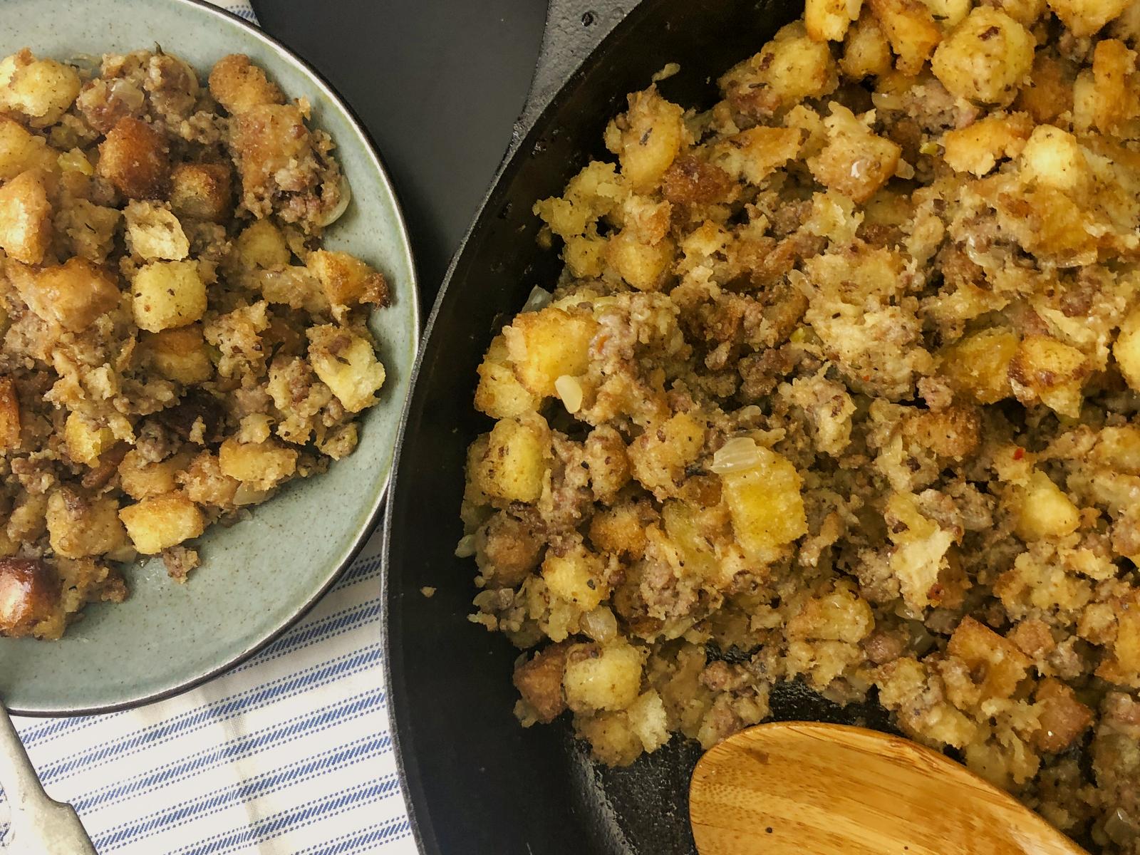 Sausage stuffing spooned onto a blue plate next to the cast iron skillet.
