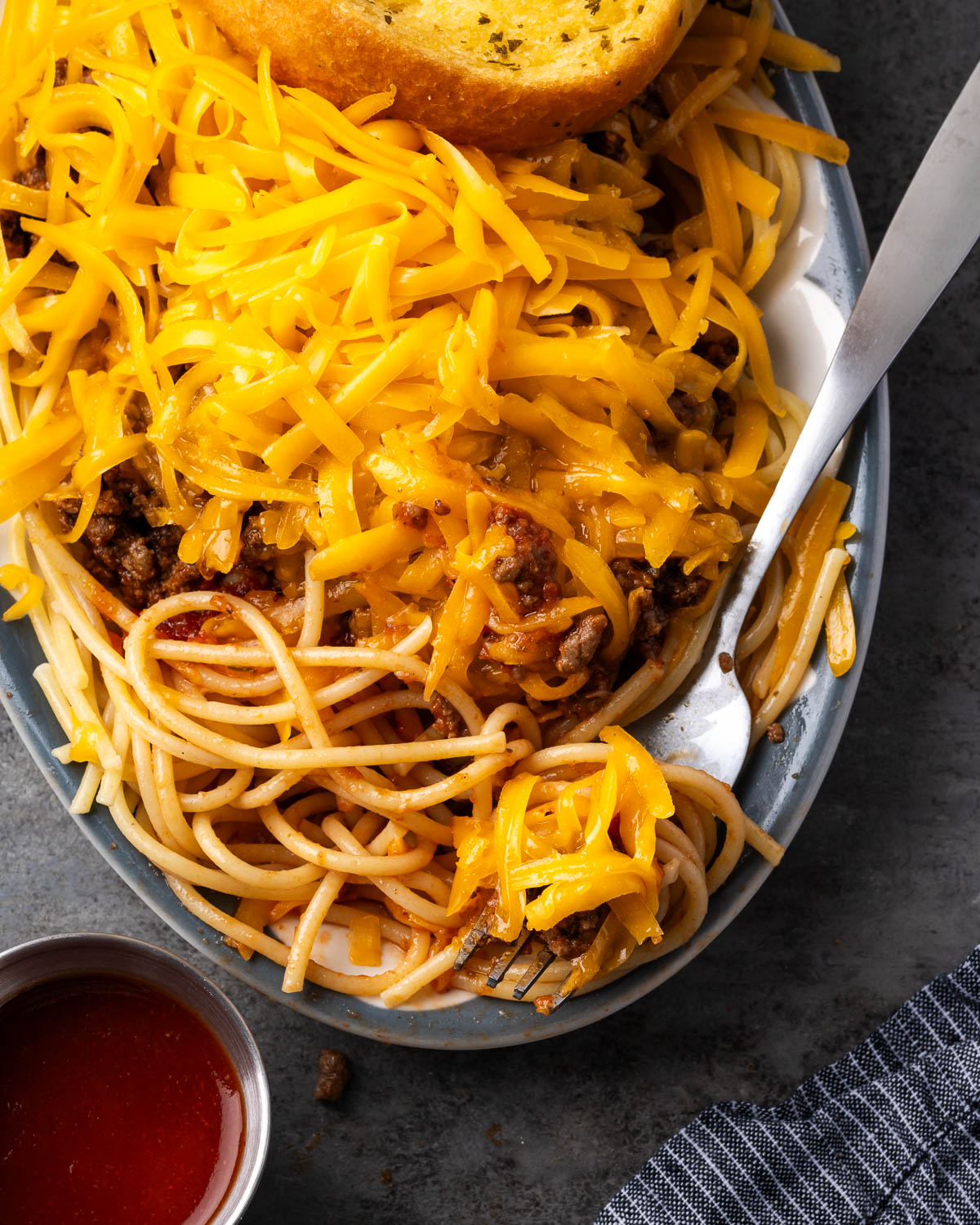 Fork lifting noodles from a plate of taco spaghetti with cheese stretching from underneath