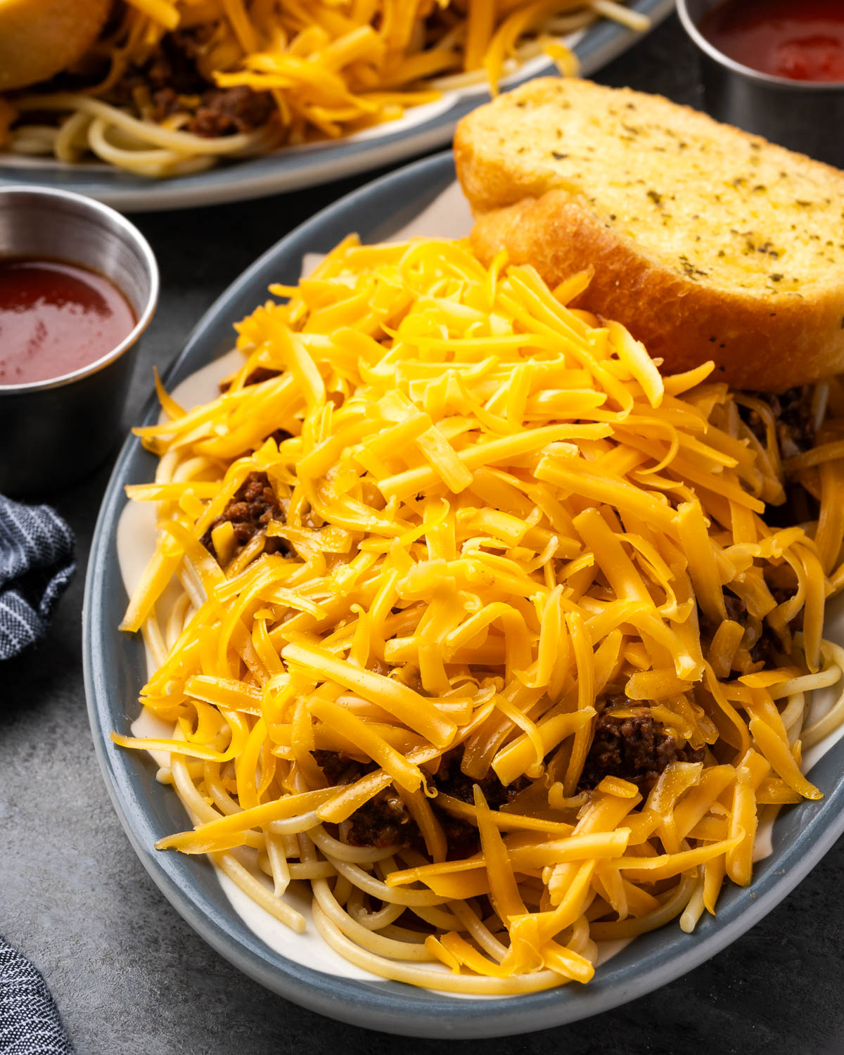 Plate of taco spaghetti topped with a mound of shredded cheddar with garlic bread alongside