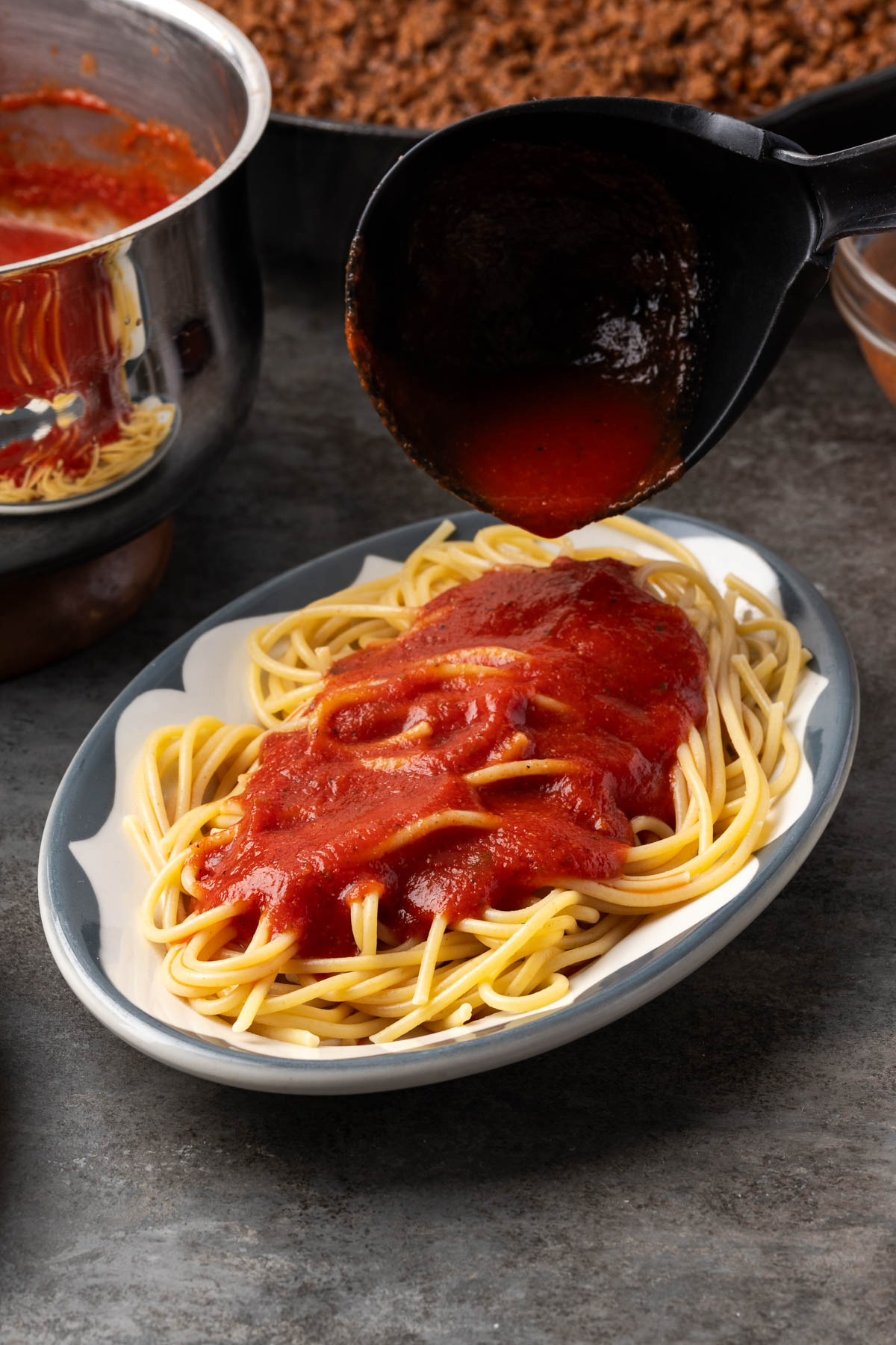 Ladling red spaghetti sauce over plain noodles on an oval diner plate