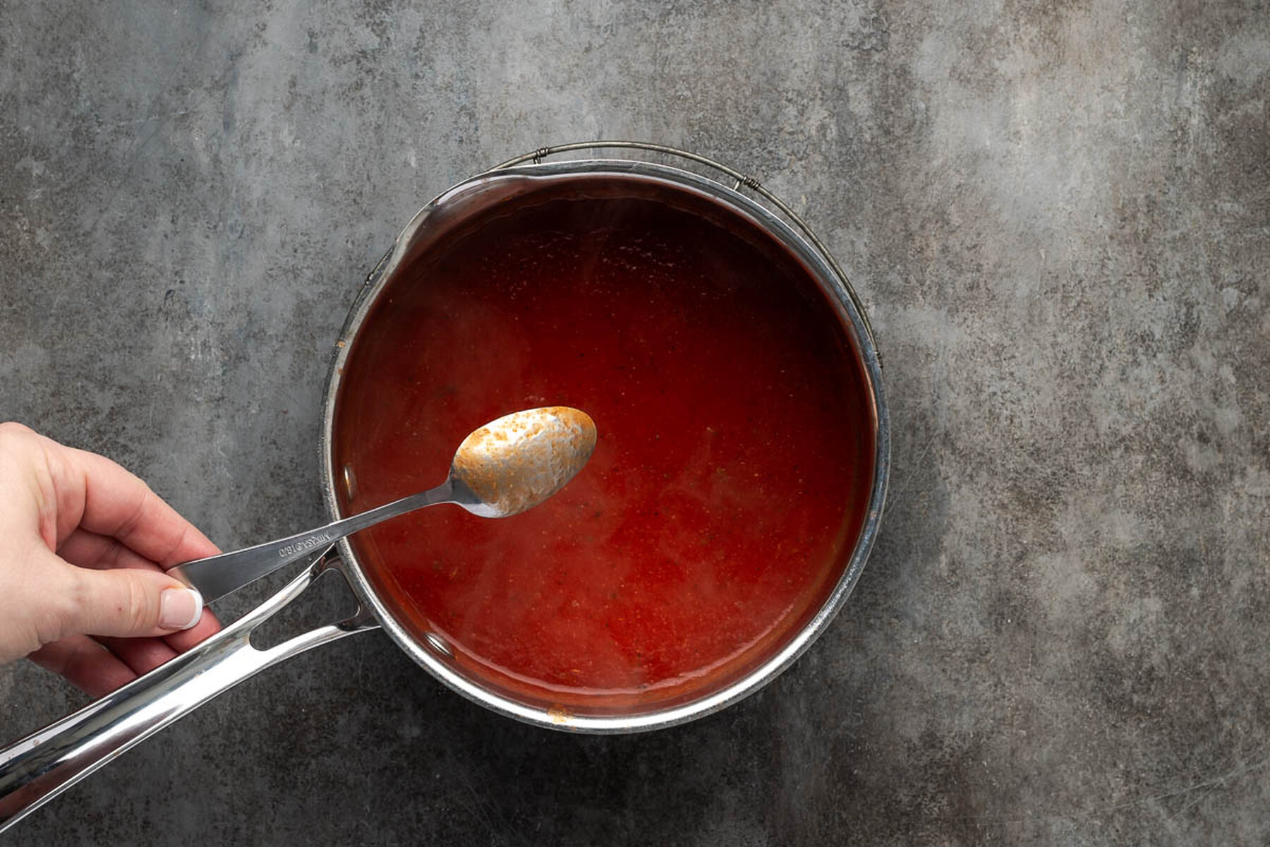 Spoon lifted from the saucepan showing the thin pourable spaghetti sauce