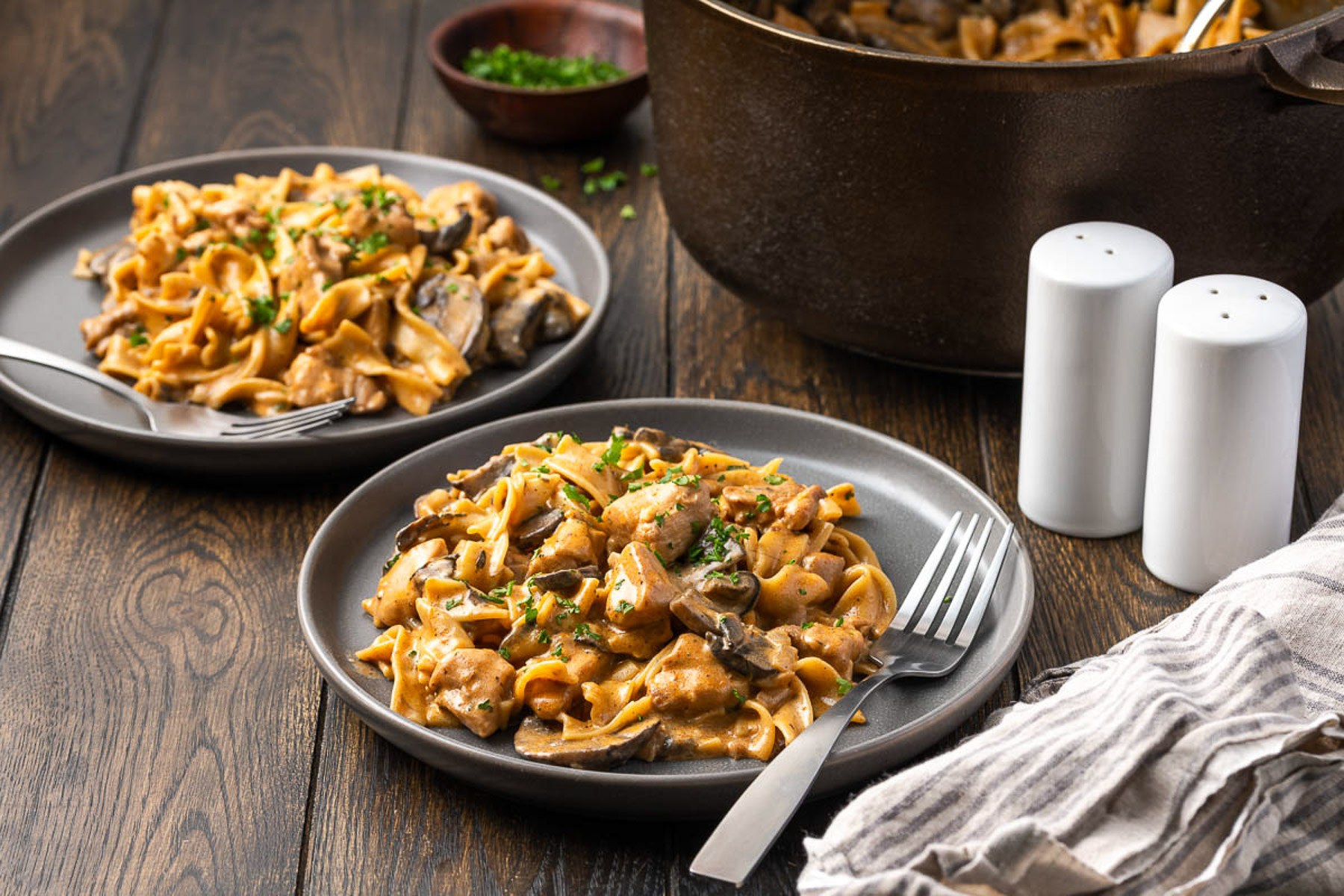 Two plates of chicken stroganoff with a cast iron Dutch oven in the background
