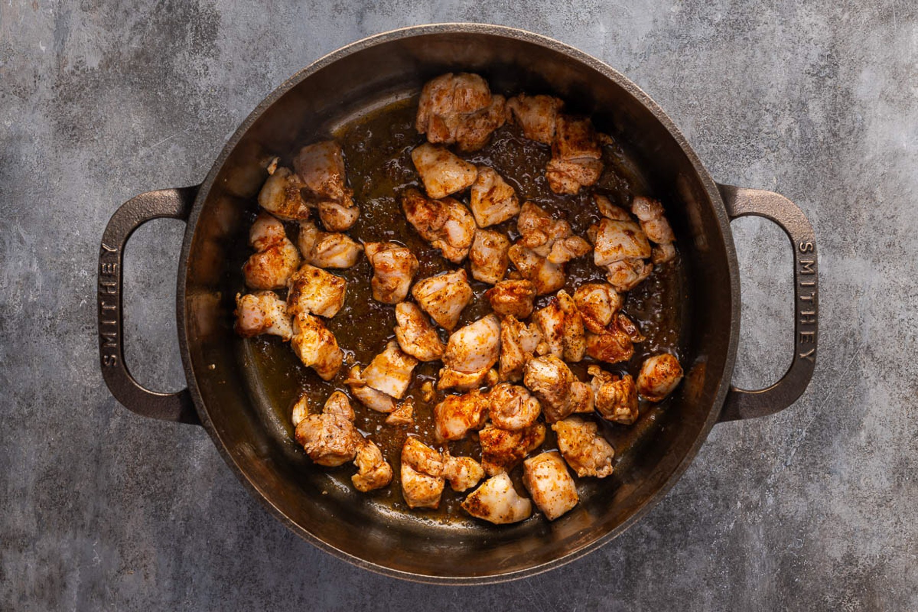 Seasoned chicken pieces searing golden brown in a cast iron Dutch oven