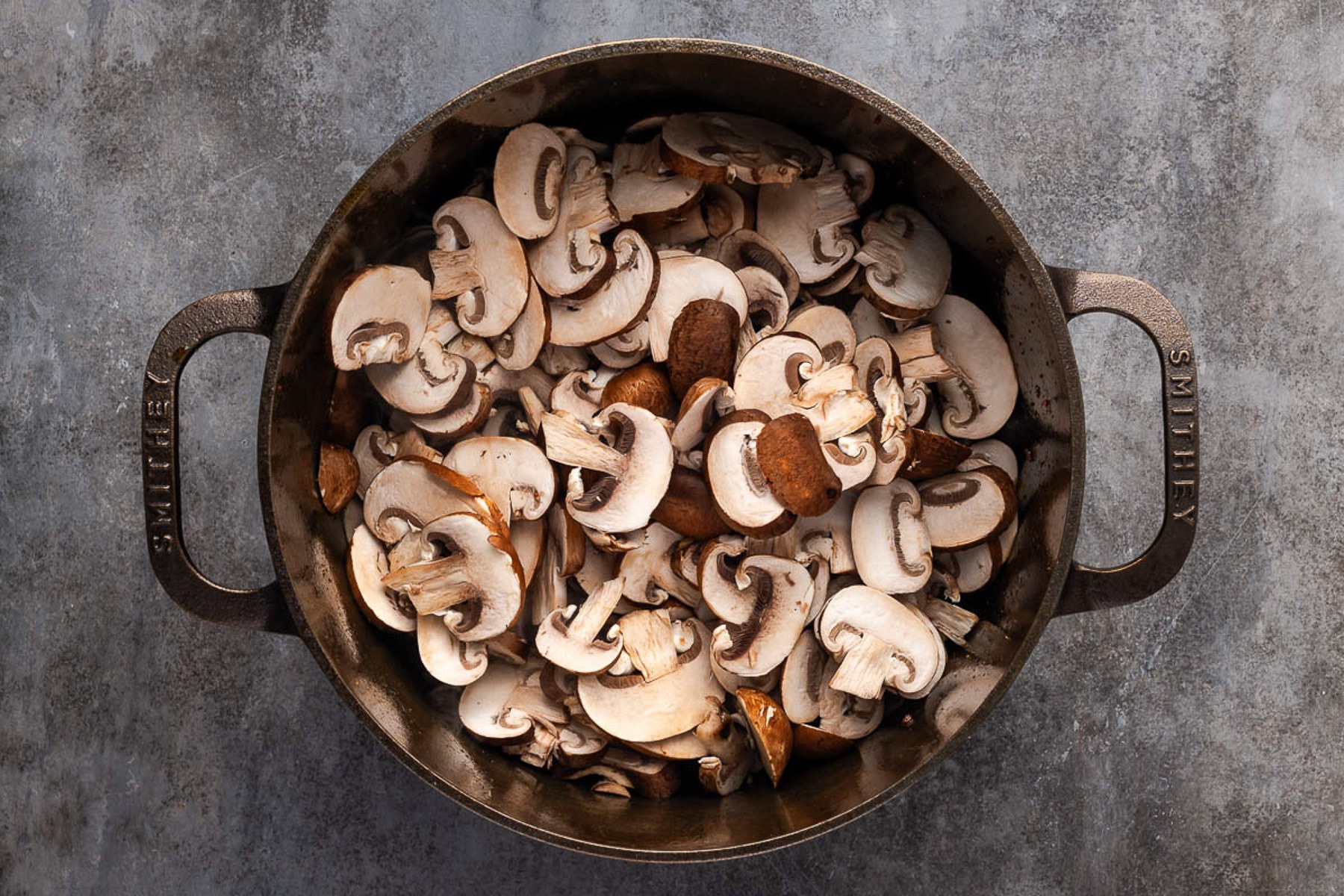 Sliced cremini mushrooms browning in a cast iron Dutch oven