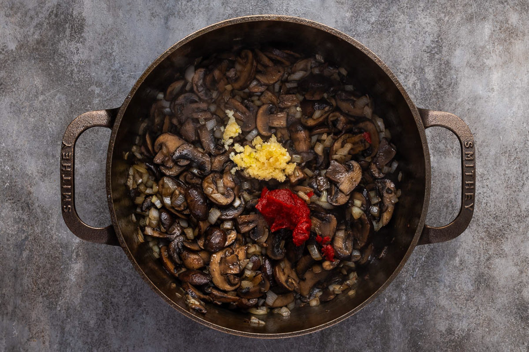 Minced garlic and tomato paste added to browned mushrooms and onion in a Dutch oven