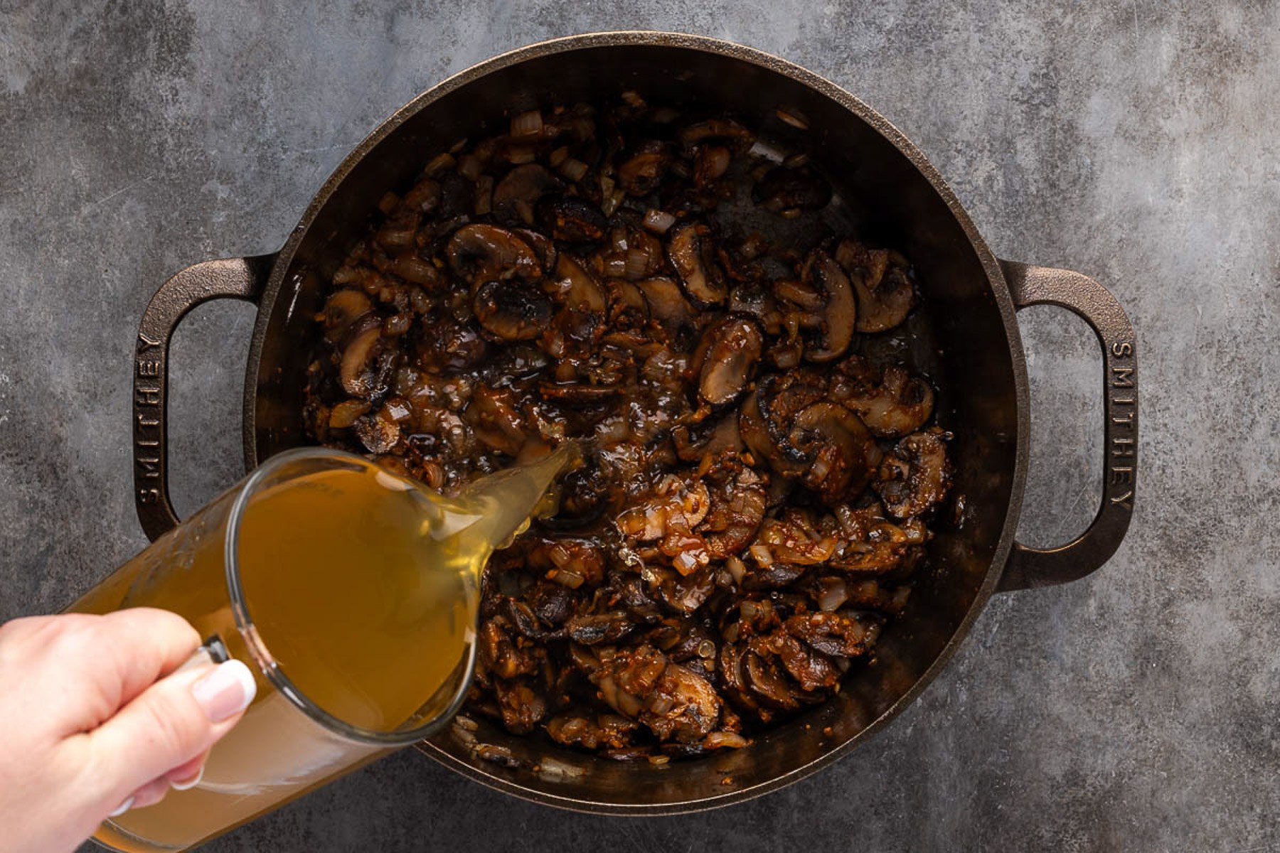 Chicken broth being poured into the Dutch oven over flour and mushrooms