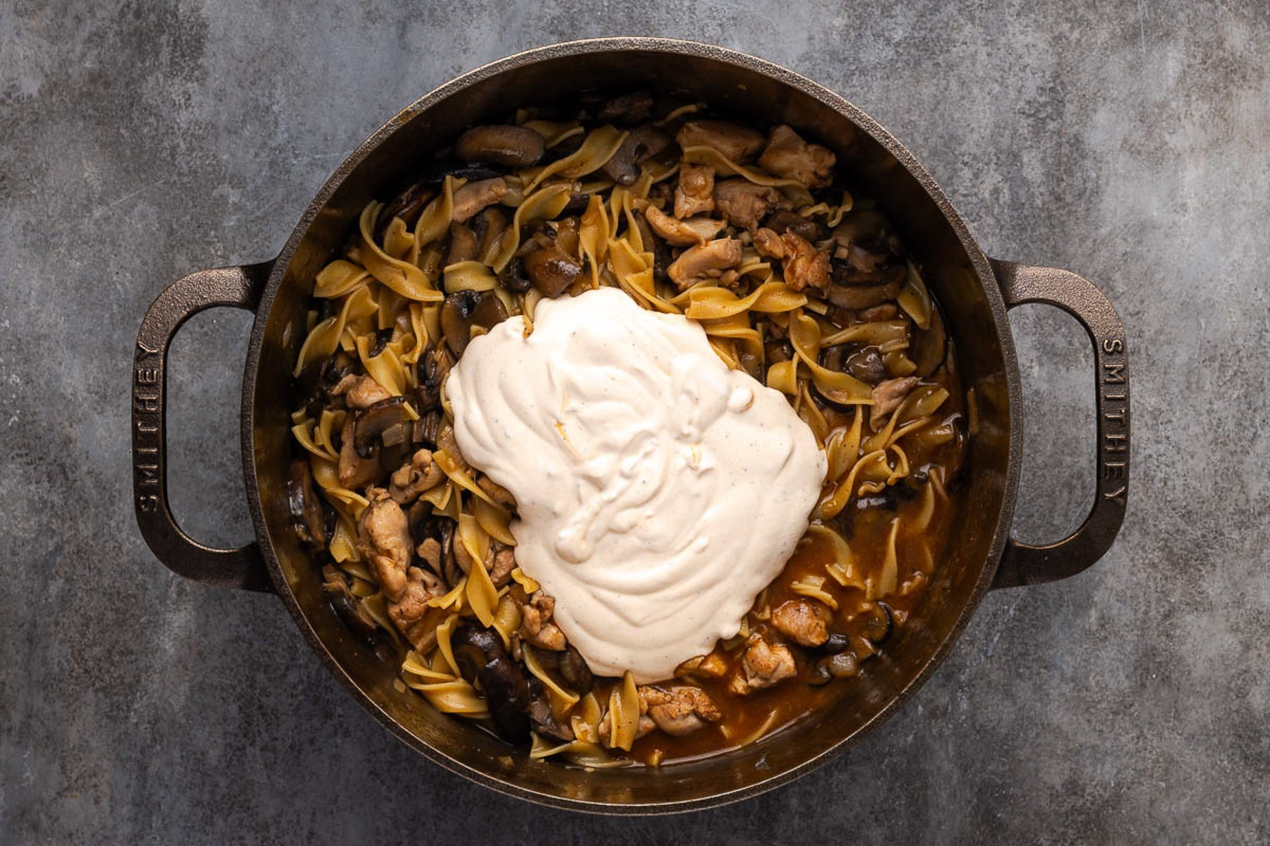 Tempered sour cream poured over the noodles and chicken in a Dutch oven